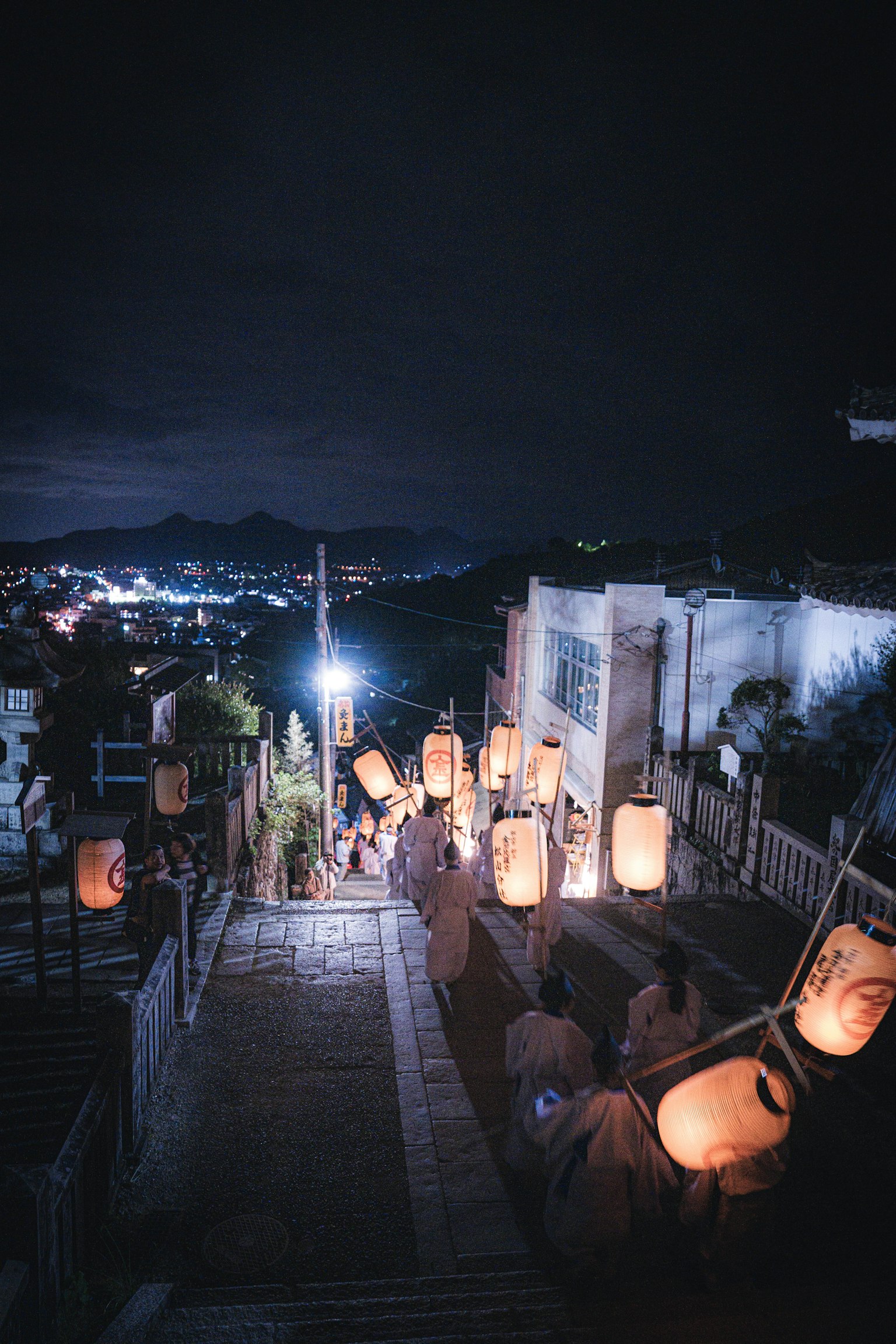 People descending illuminated stairs at night with lanterns