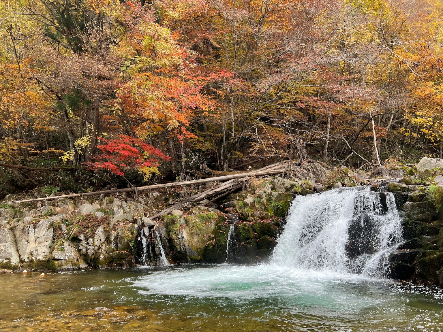 A small waterfall surrounded by vibrant autumn leaves and calm water