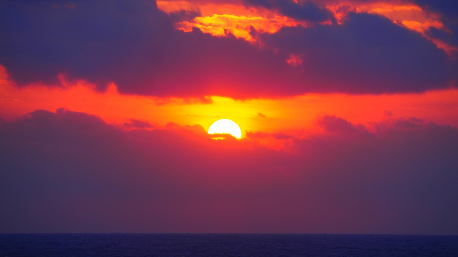Sonne, die über dem Ozeanhorizont mit lebhaft rotem Himmel untergeht