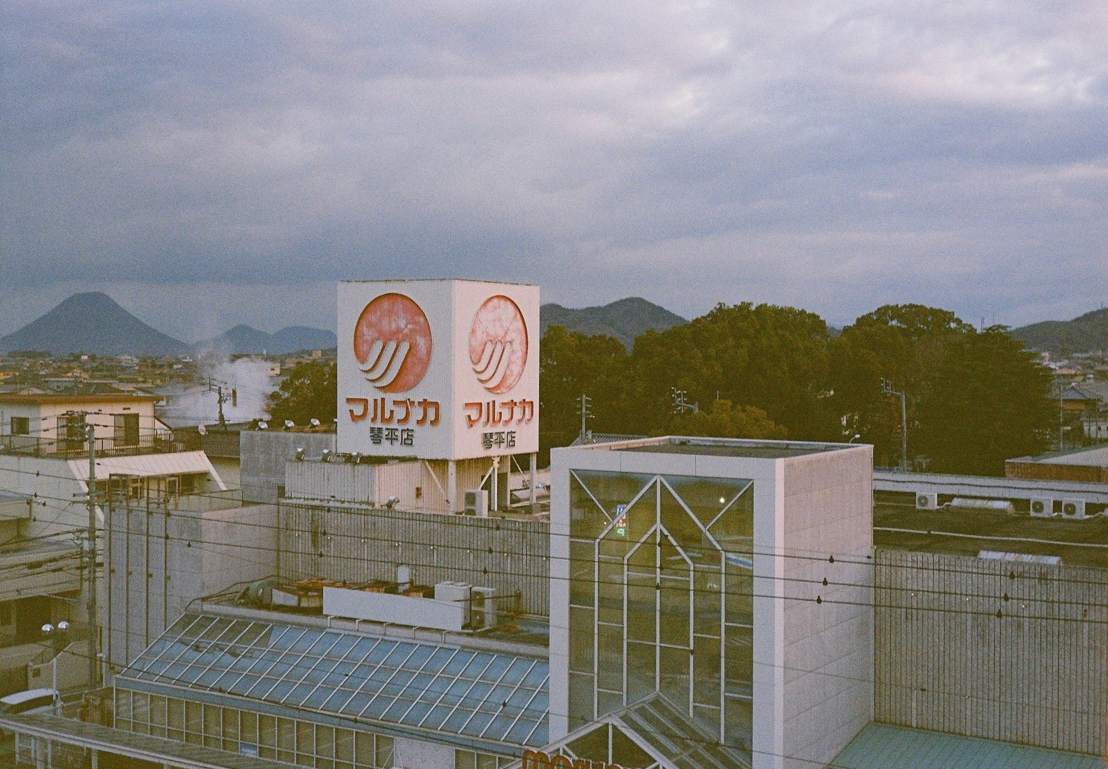 夕暮れの街並みと山々の背景にある商業ビルの屋上看板