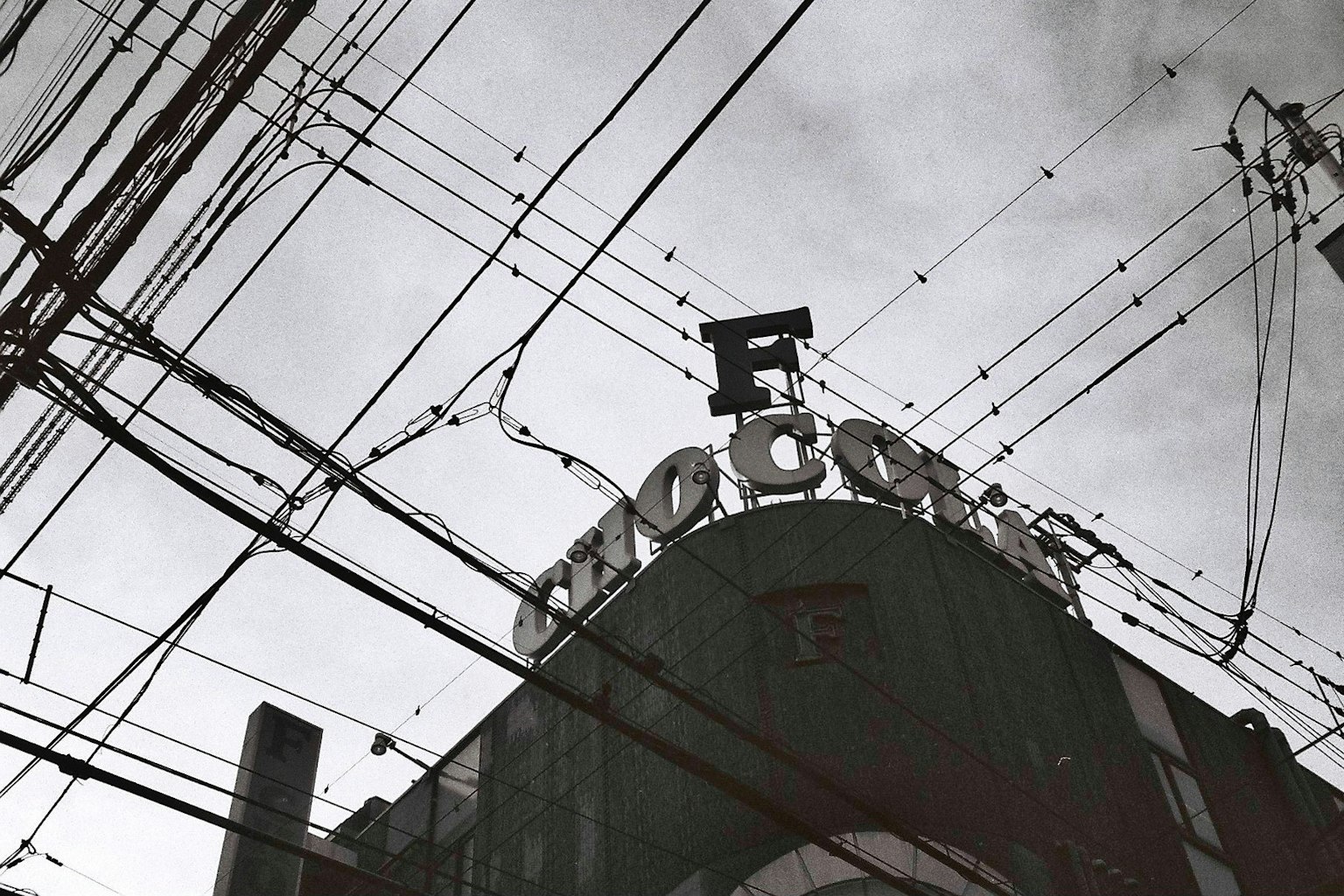 Black and white photo featuring a prominent sign with the letter F atop a building surrounded by power lines