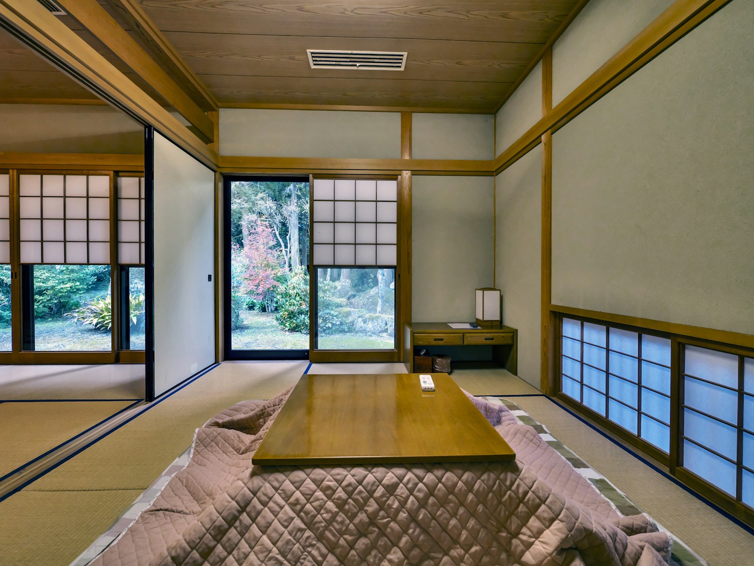 Innenraum eines traditionellen japanischen Zimmers mit einem Holztisch und Kissen mit Blick auf einen Garten