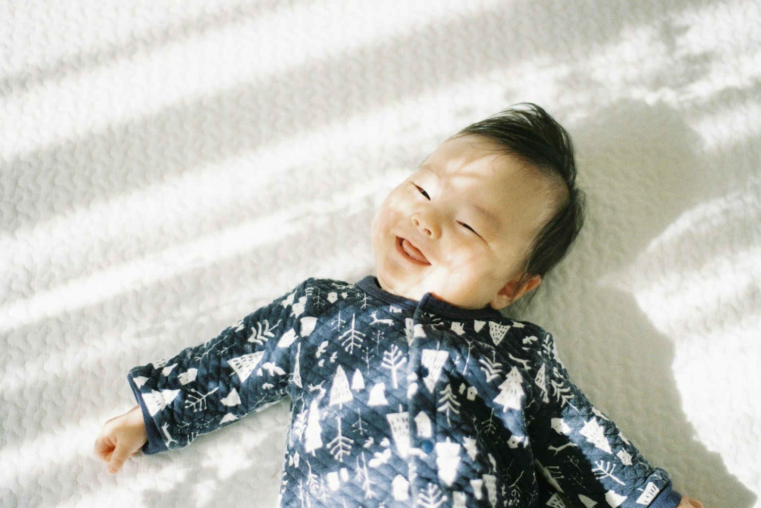 ทารกยิ้มอยู่บนพื้นผิวสีขาวมีแสงนุ่มนวลและเงา
