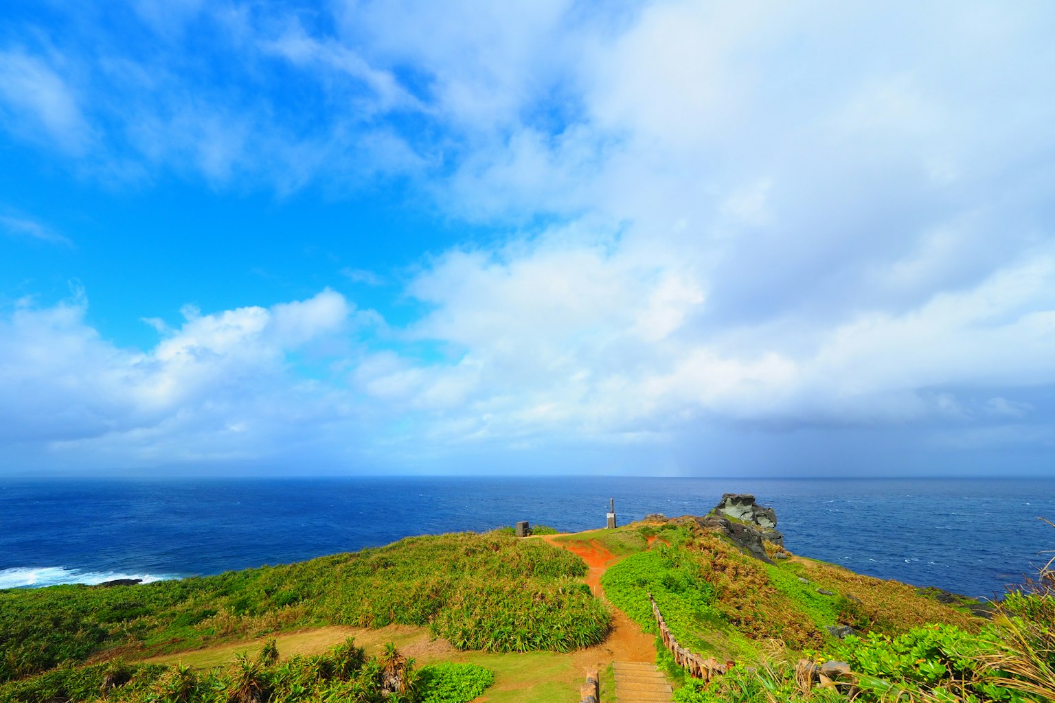 Scenic view of a green hillside against a blue sky and ocean