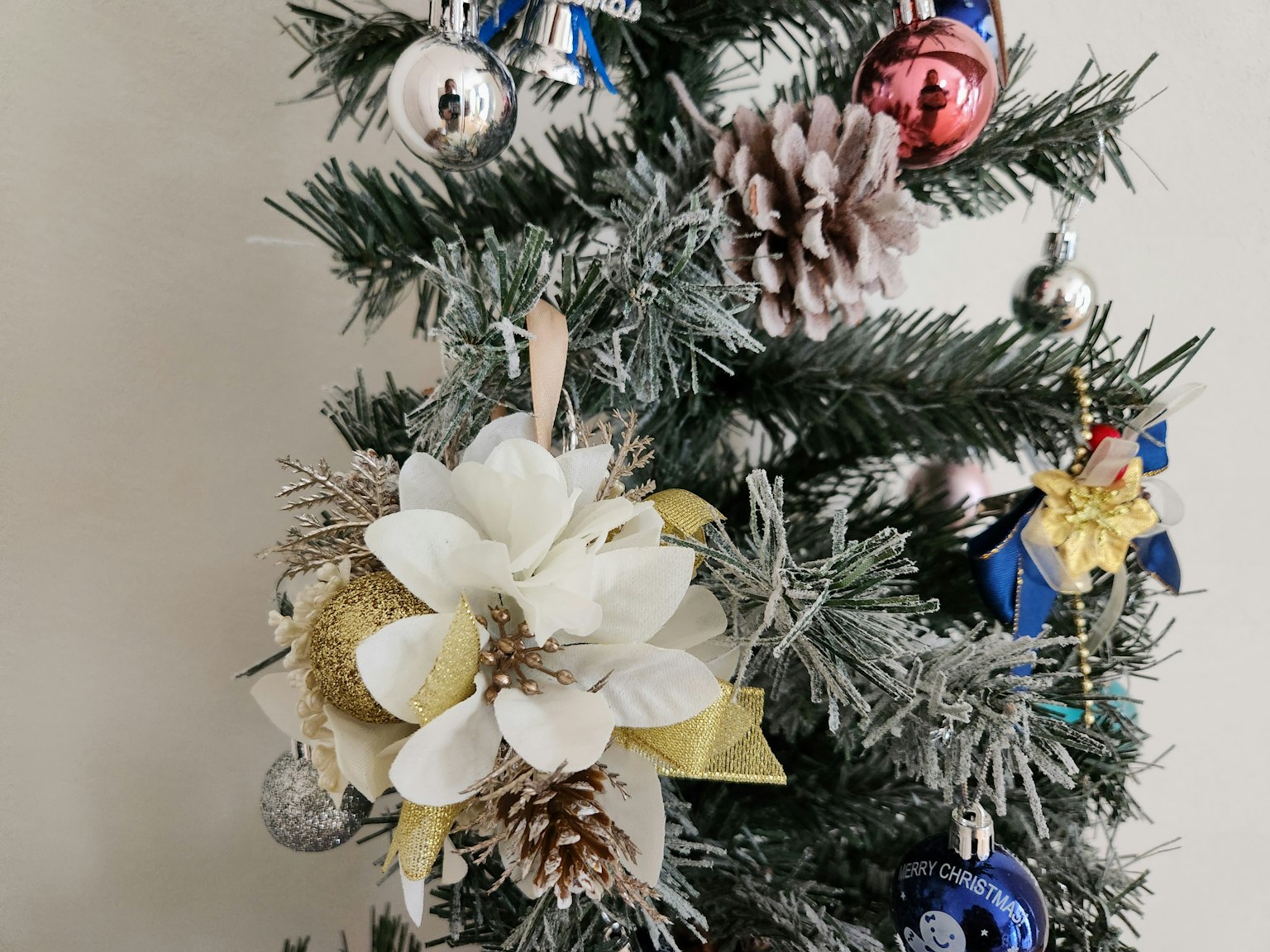 Weihnachtsbaum dekoriert mit einer weißen Blume und Tannenzapfen mit roten und blauen Ornamenten