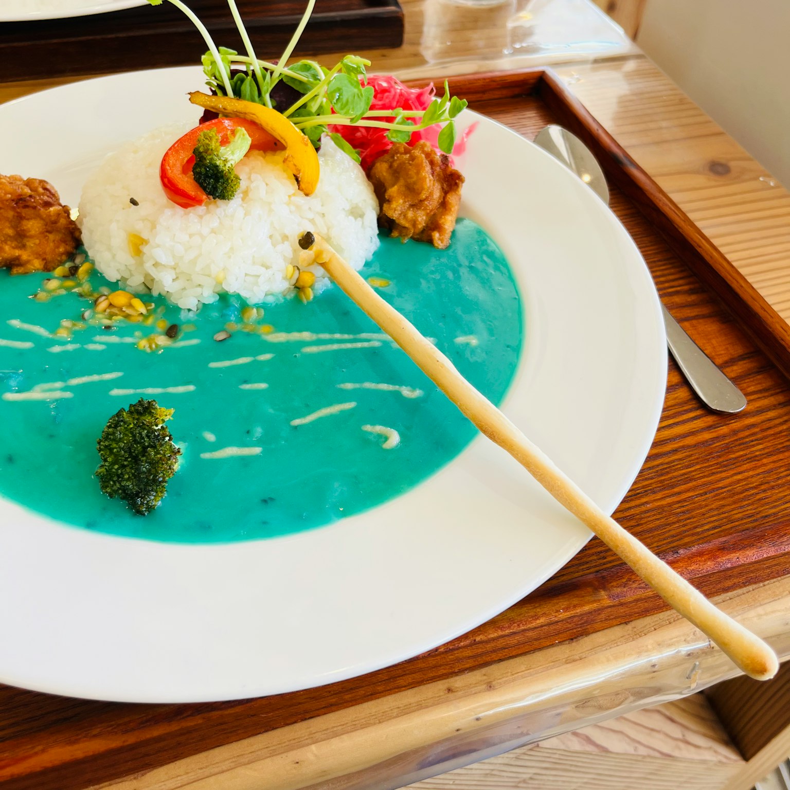 Piring dengan nasi dalam sup biru dan sayuran serta batang bambu