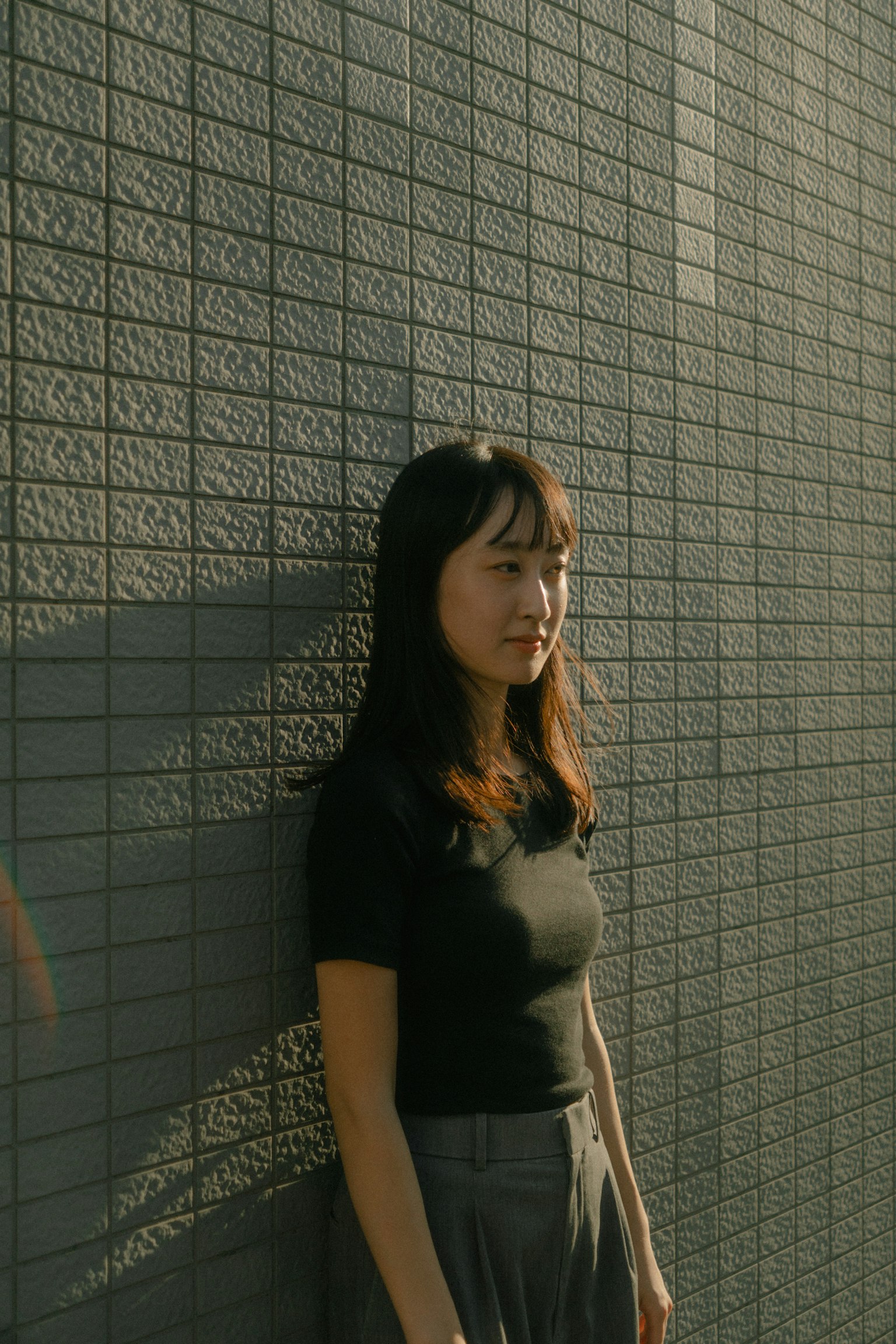一个女人靠在墙上，在自然光中露出放松的表情