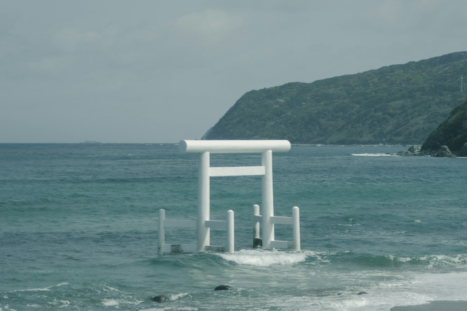 Weißes Torii im Ozean mit grünen Bergen im Hintergrund