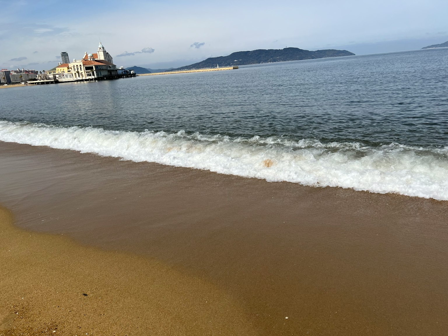 Plage de sable avec des vagues et une mer calme en arrière-plan avec des bâtiments et des montagnes