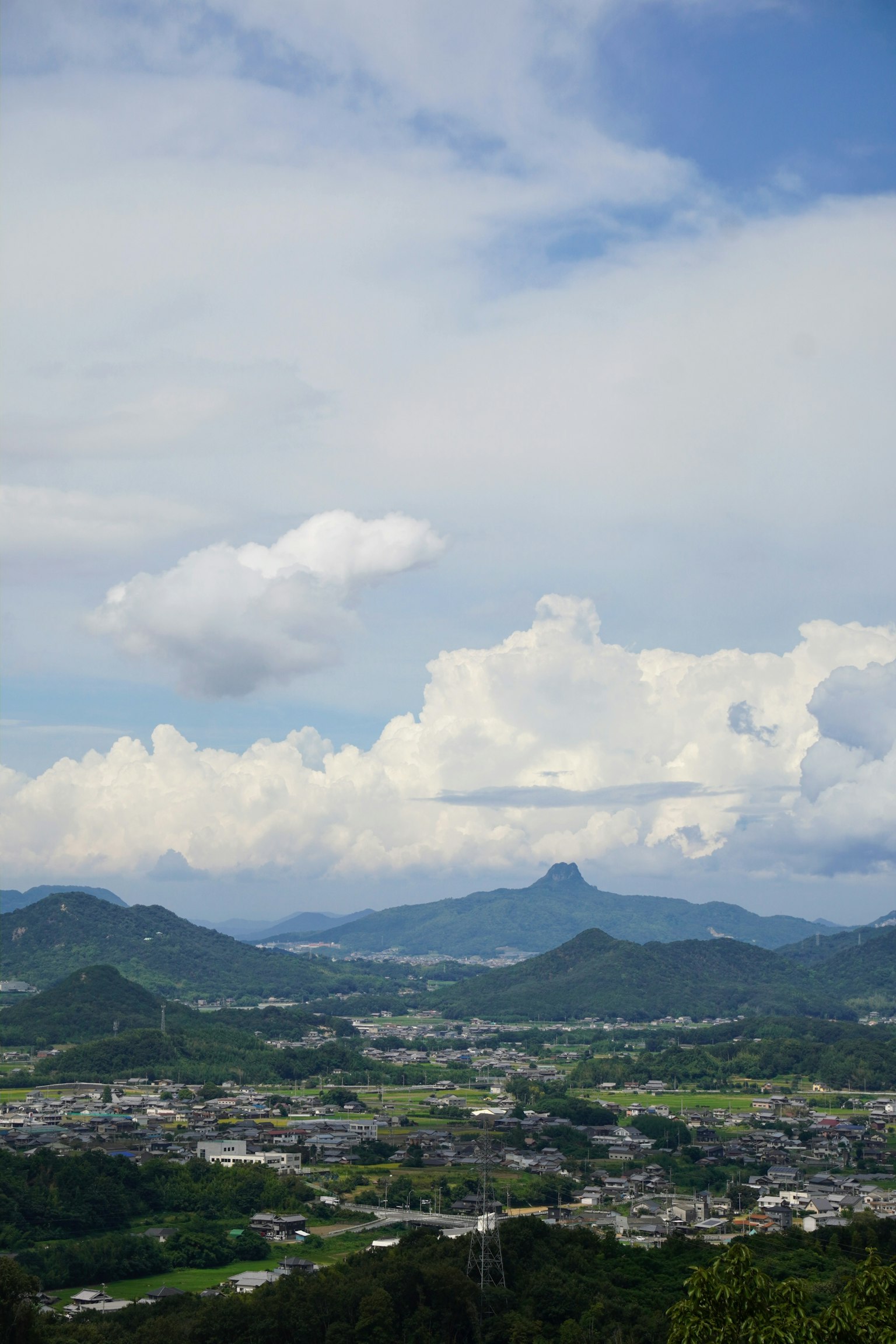 Vista escénica de montañas bajo un cielo azul con nubes blancas colinas verdes y una ciudad en primer plano