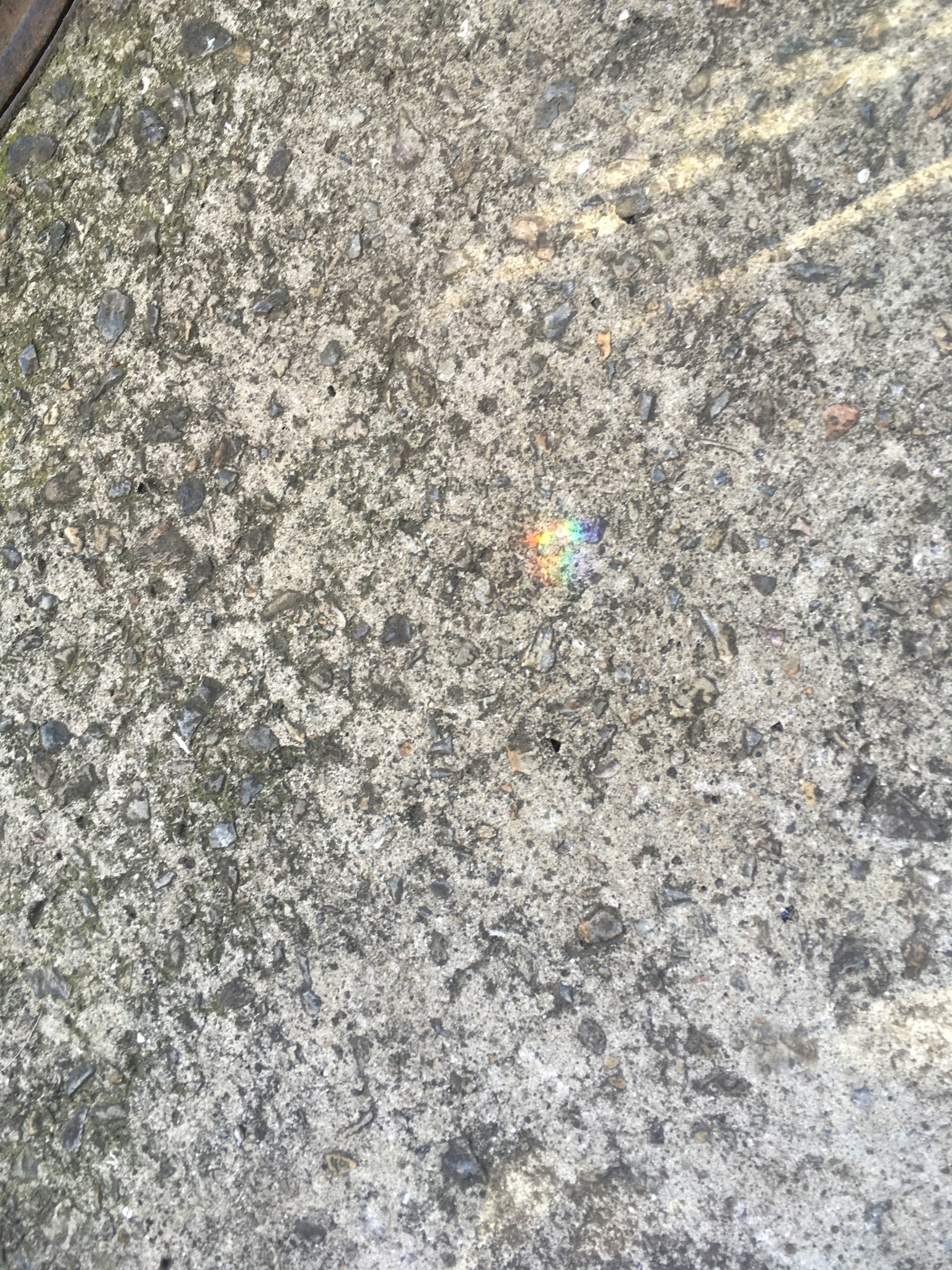 Nahaufnahme einer Betonoberfläche mit einem kleinen regenbogenfarbenen Fleck