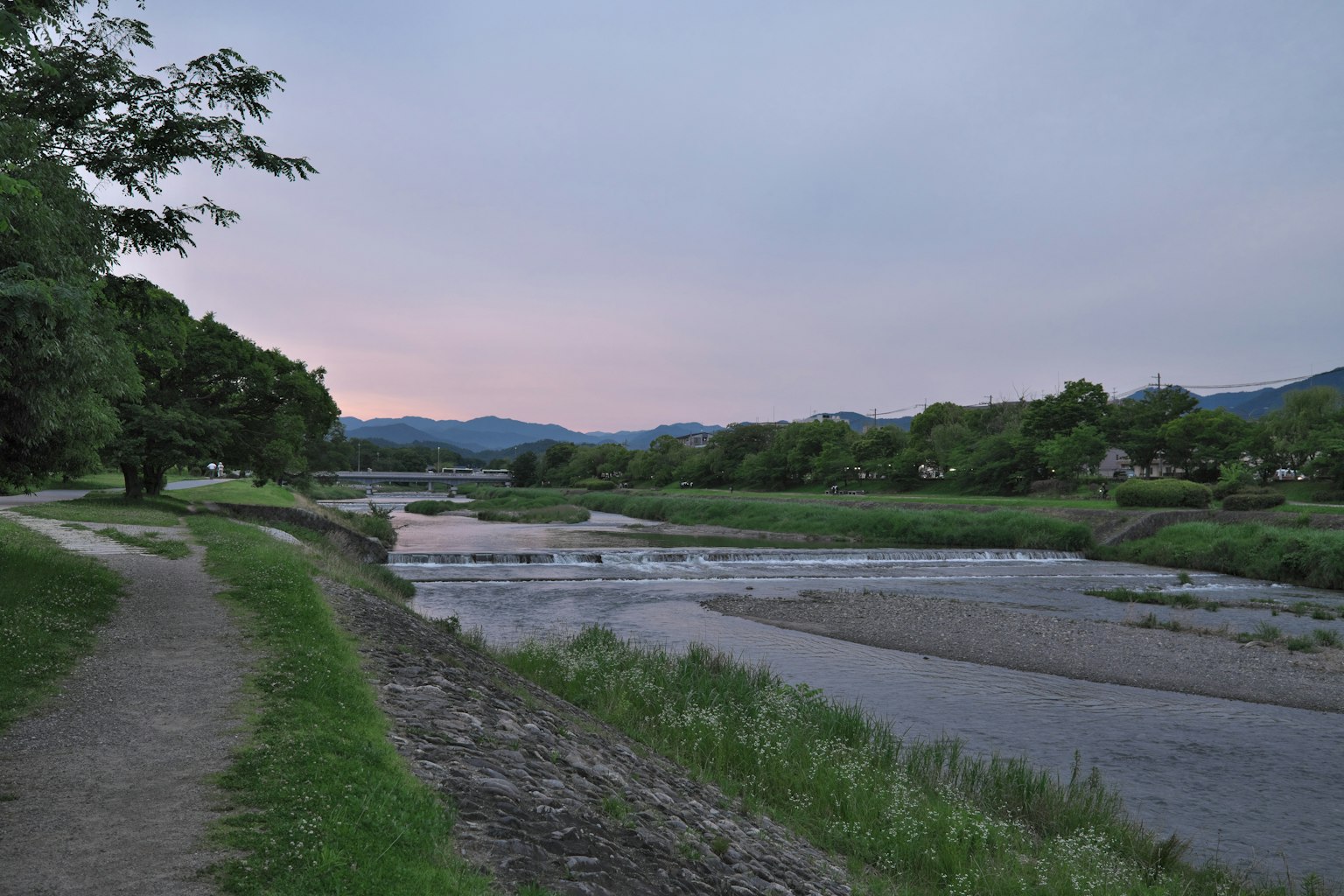 Serene riverside scene at dusk with a colorful sky and lush greenery