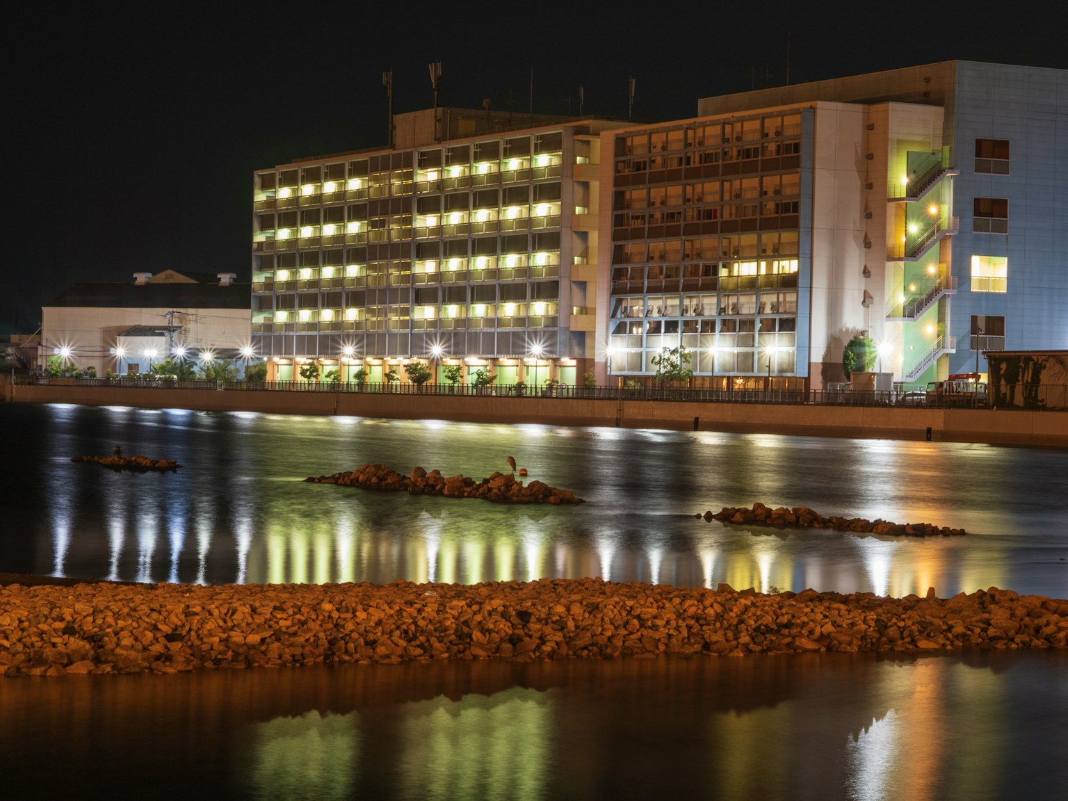 Helles Gebäude am Meer bei Nacht mit ruhiger Wasseroberfläche