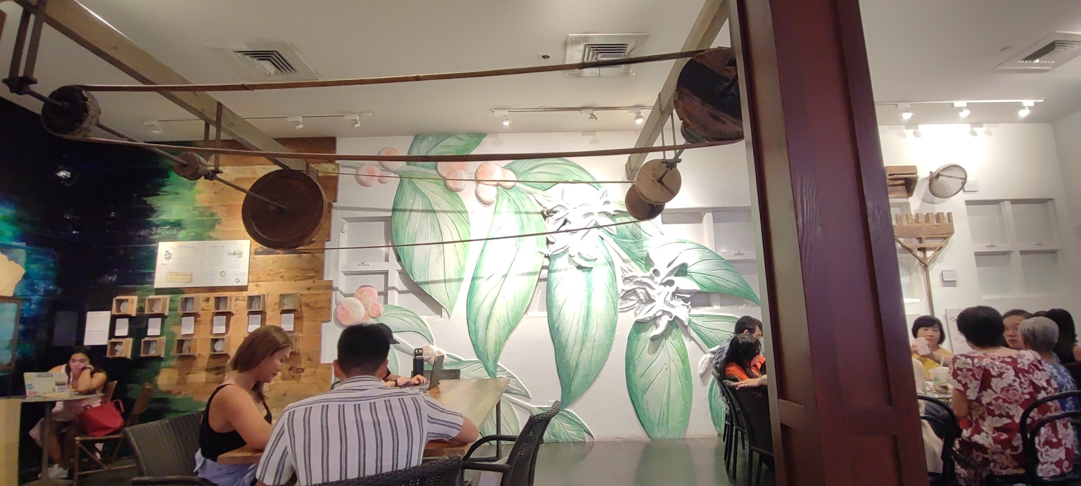 Interior de un café con un mural verde y clientes