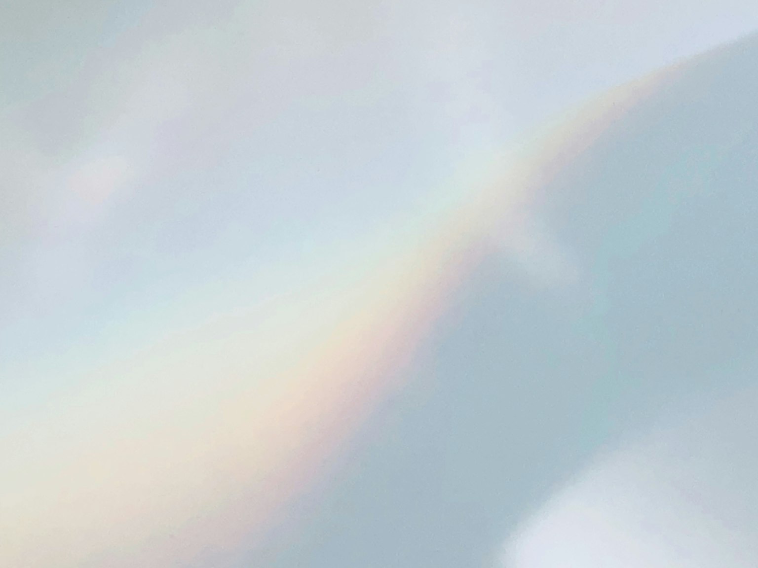 A soft-colored rainbow arching across a cloudy sky