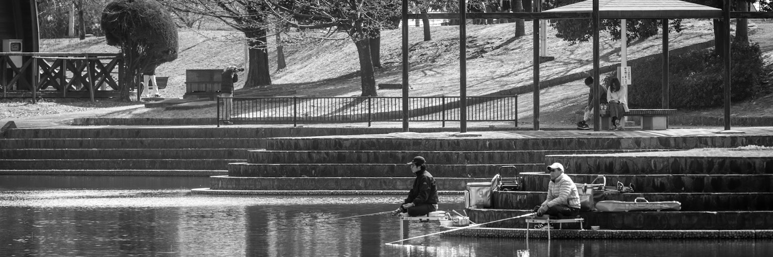 Due uomini che pescano in un parco con una superficie d'acqua serena in bianco e nero