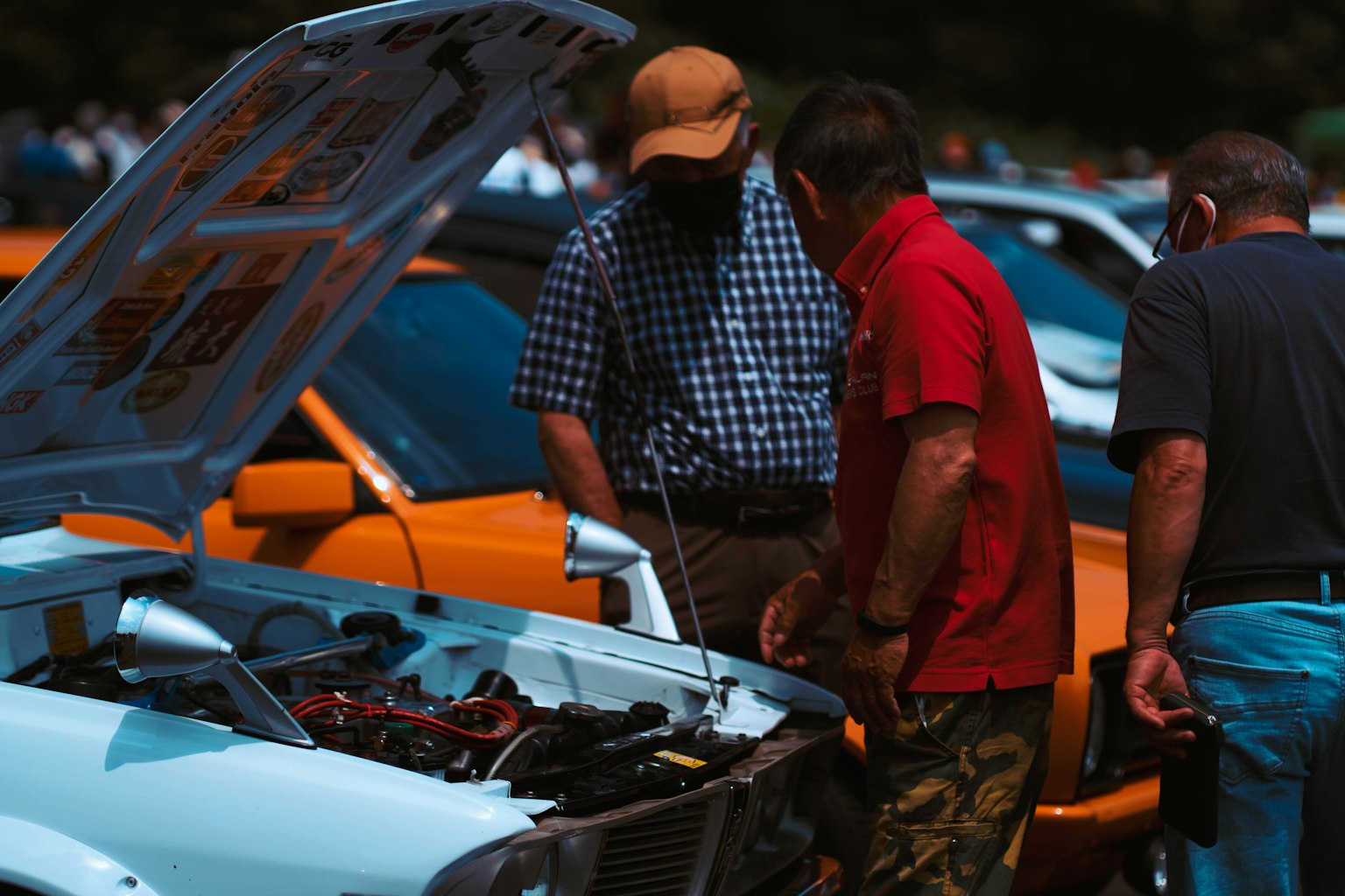 Group of men gathered around an open hood of a blue car