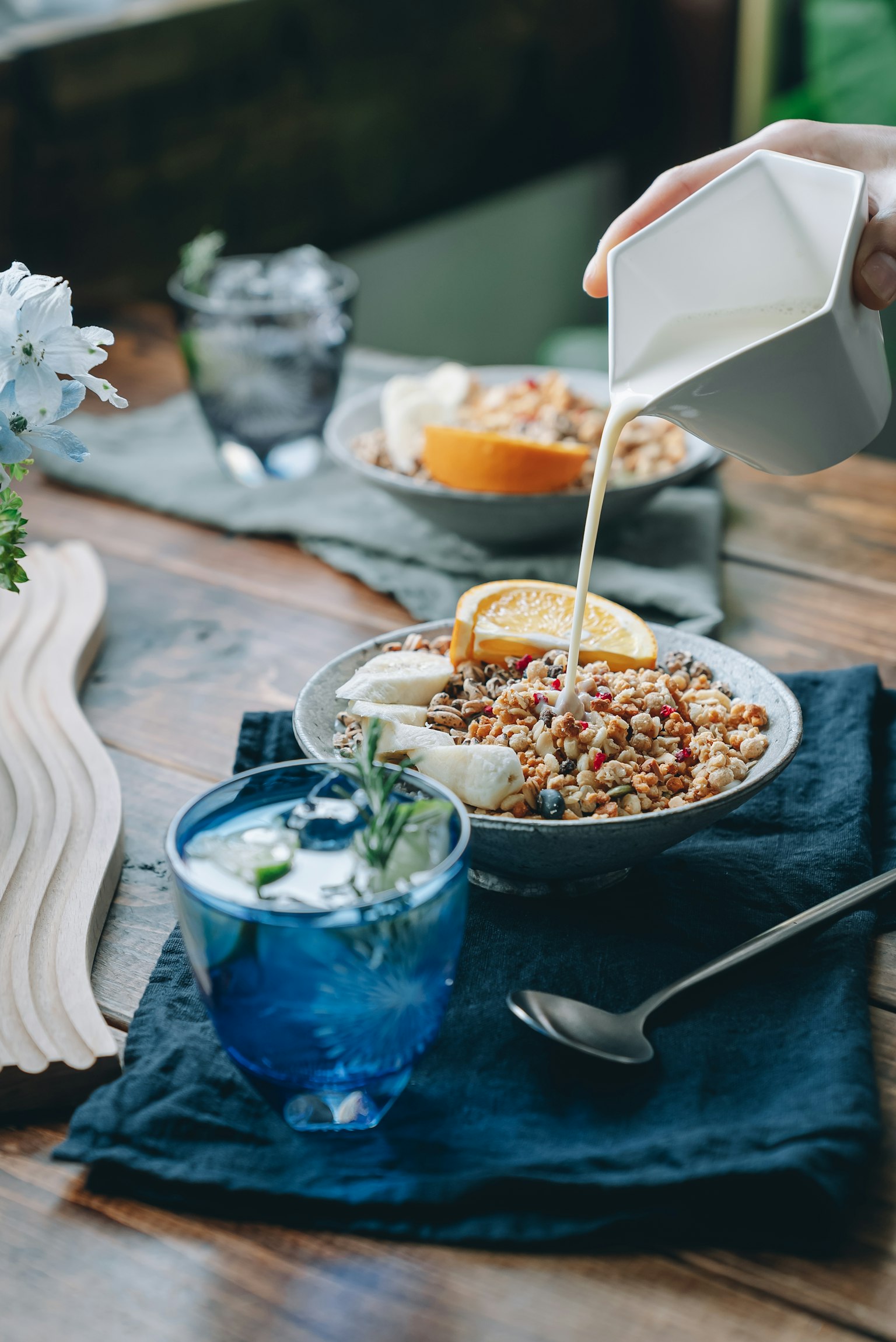Main versant du lait dans un bol de granola avec des fruits sur une table en bois