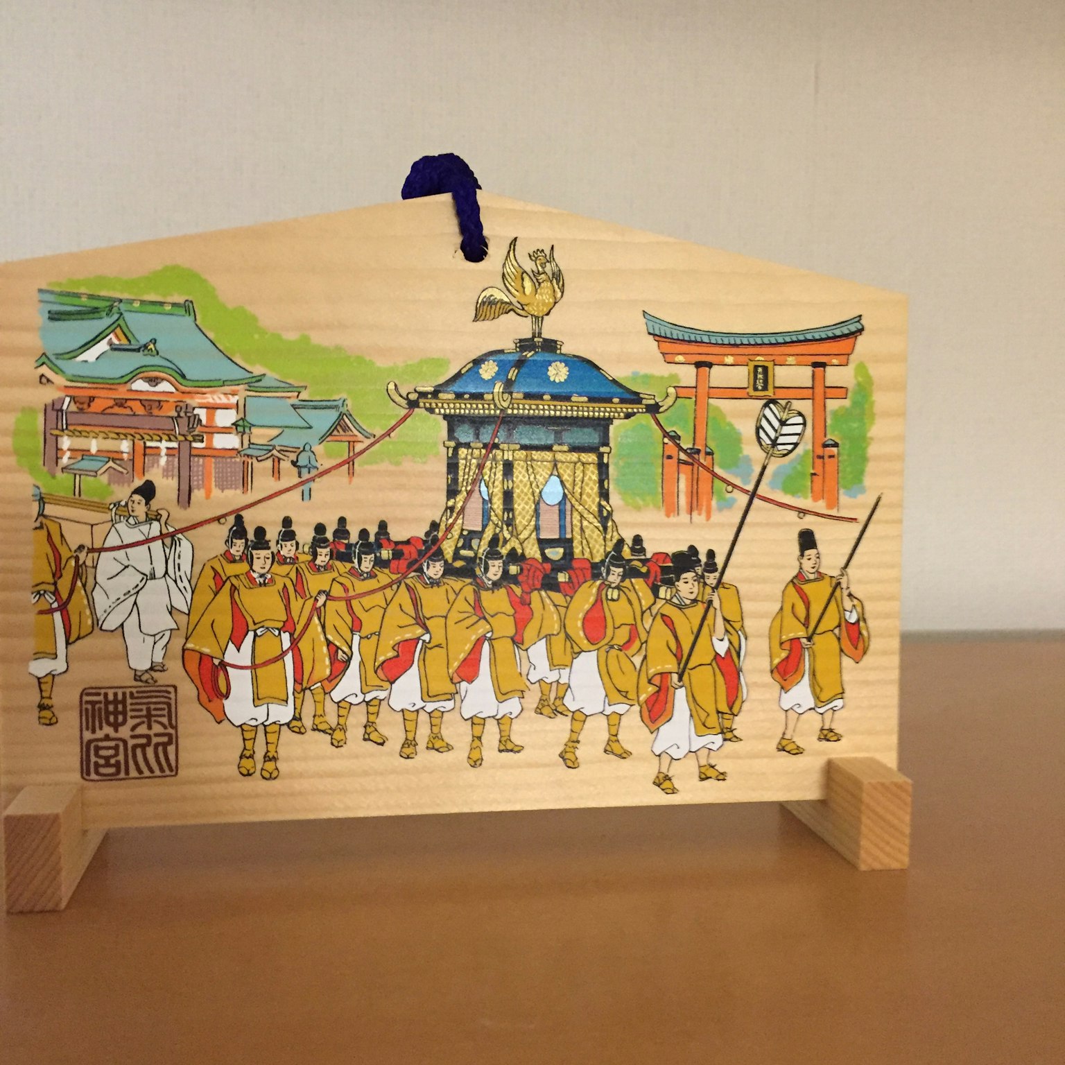 Wooden sign depicting a festival procession with people in yellow attire pulling a portable shrine