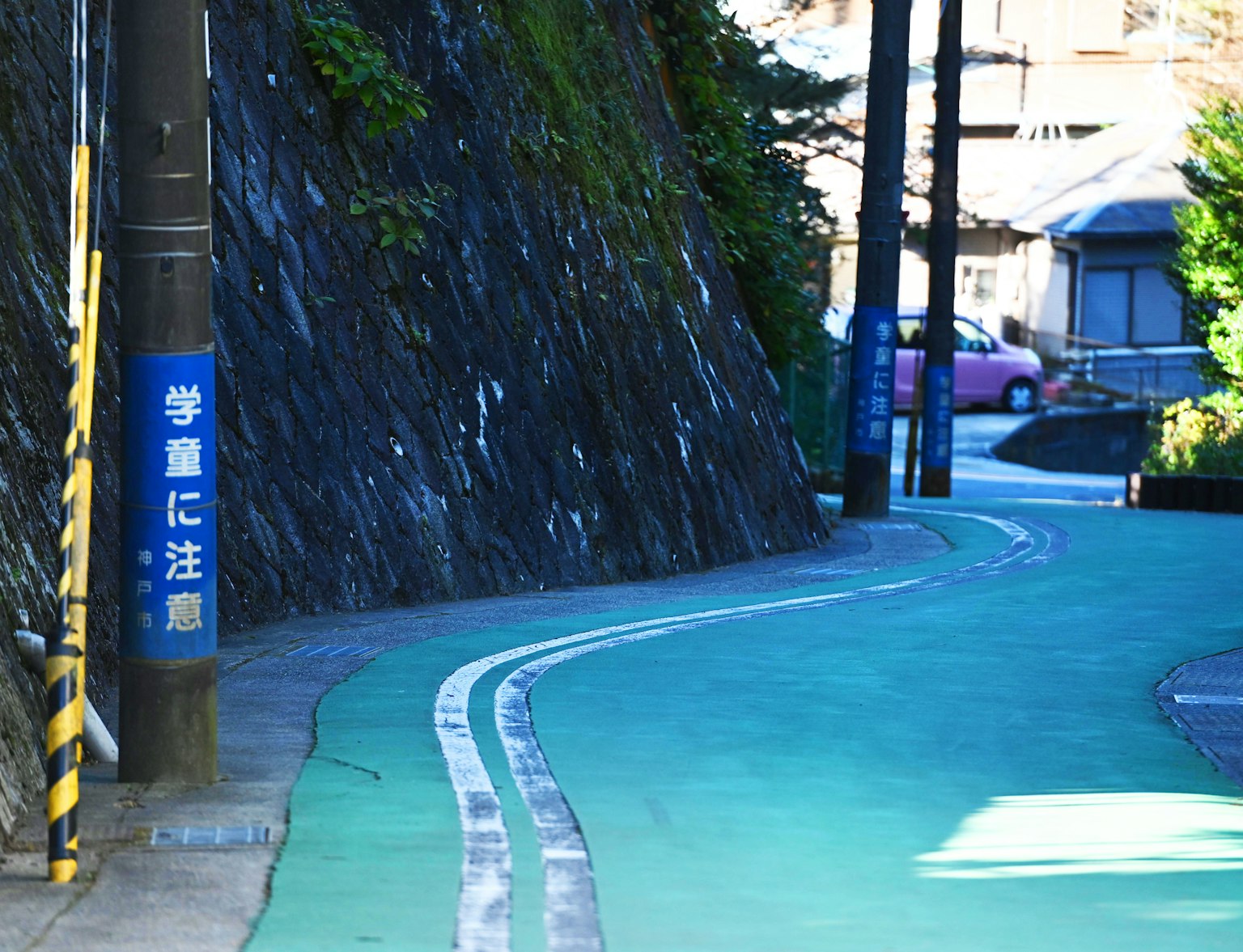 Camino verde curvado cerca de una pared de roca con un letrero de advertencia