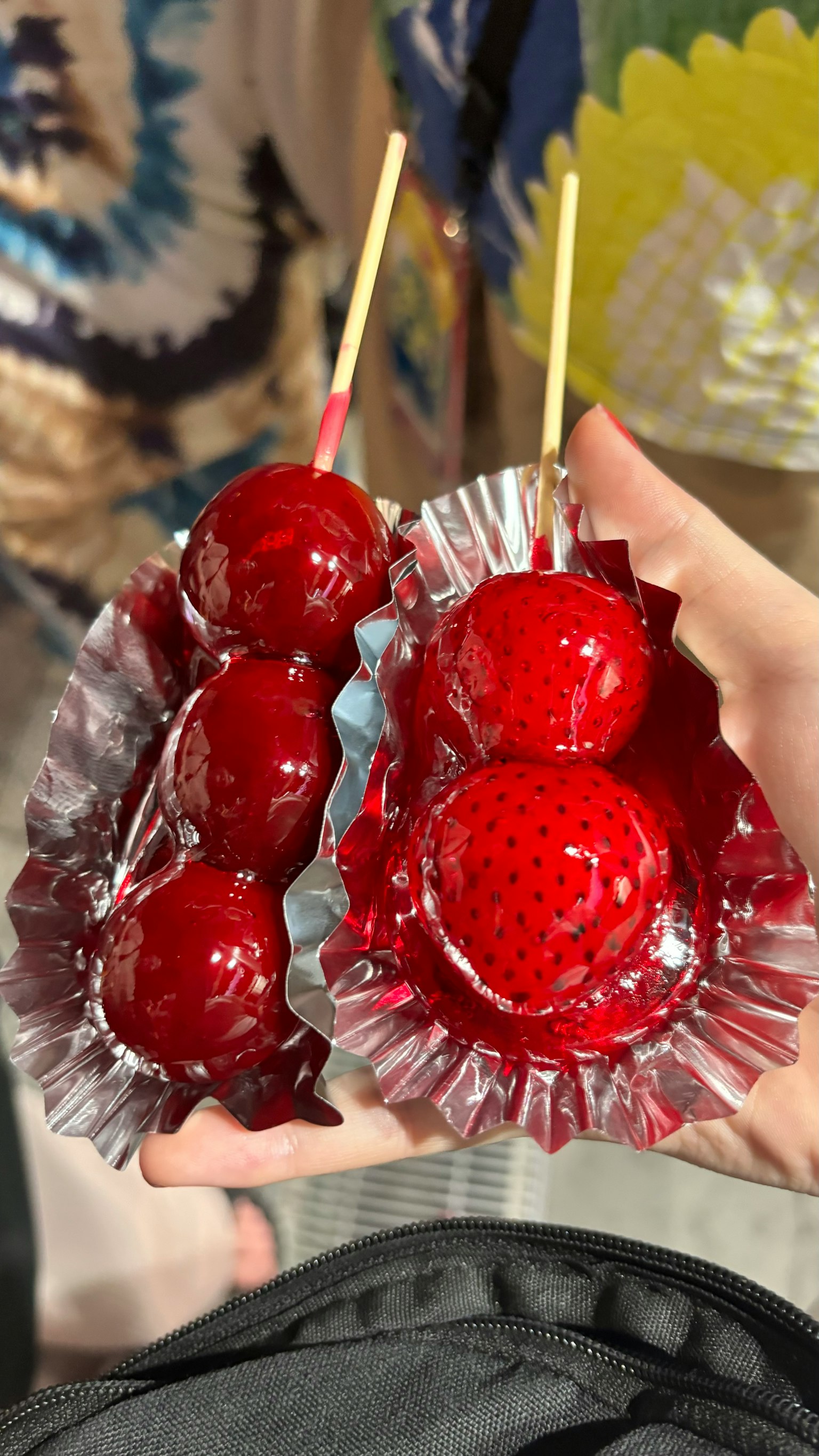 Hand holding two skewers of red candy-coated strawberries