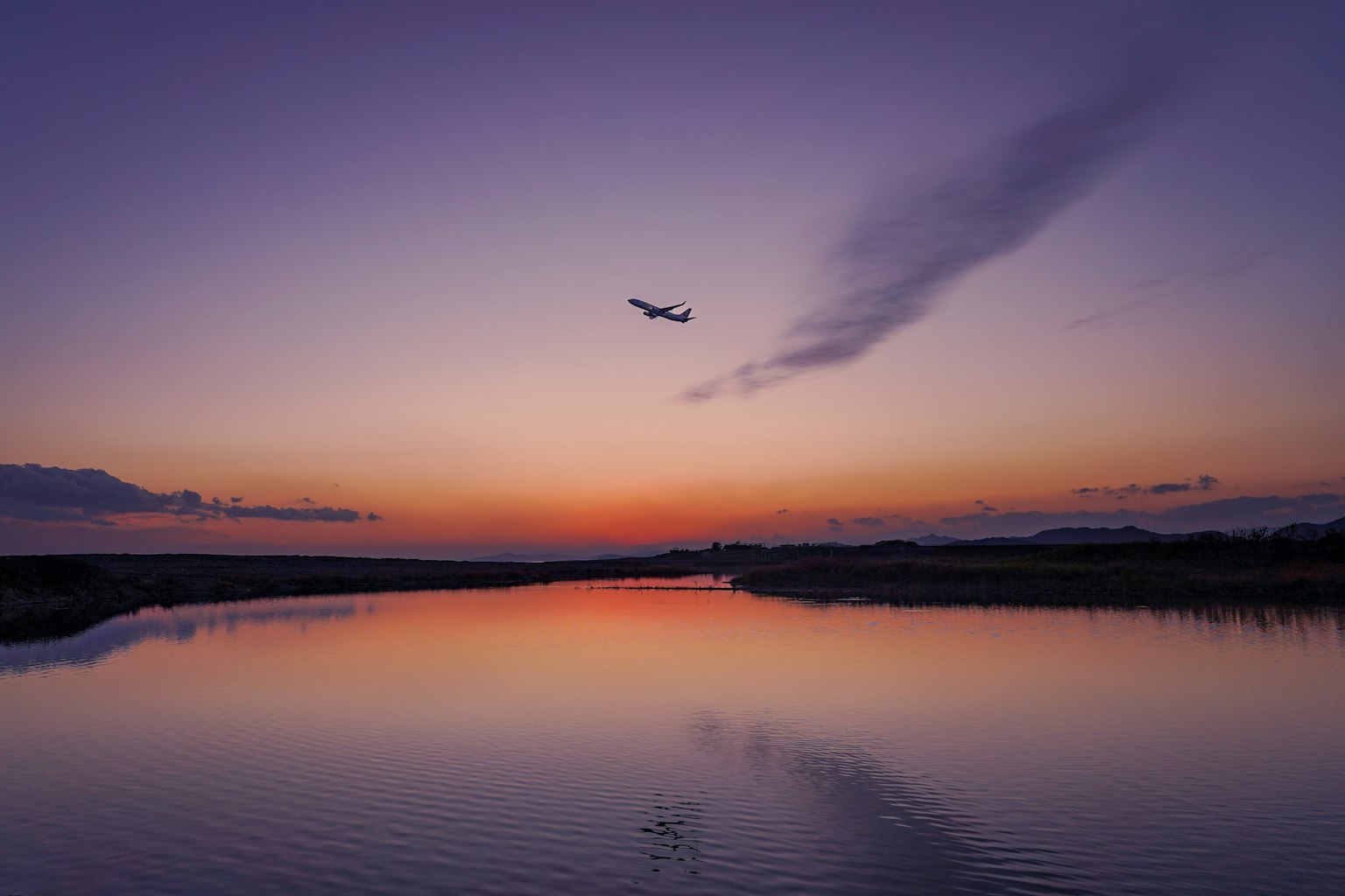 A serene lake landscape with an airplane flying in the sunset sky