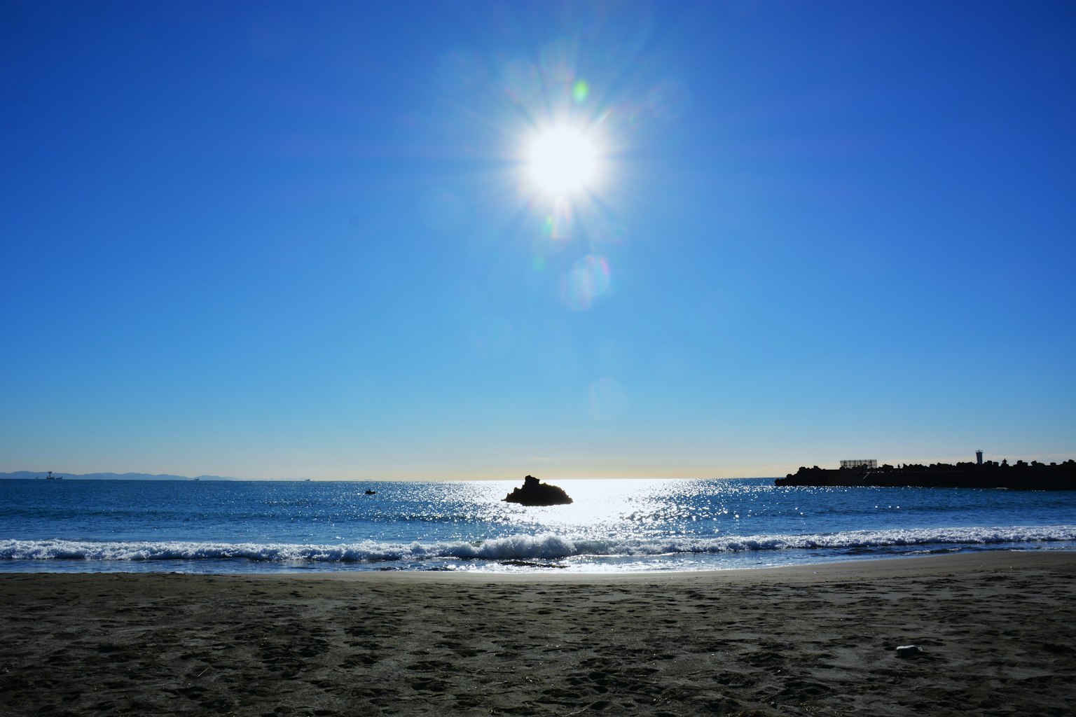 Heller blauer Himmel mit strahlender Sonne über ruhigen Meereswellen und Sandstrand