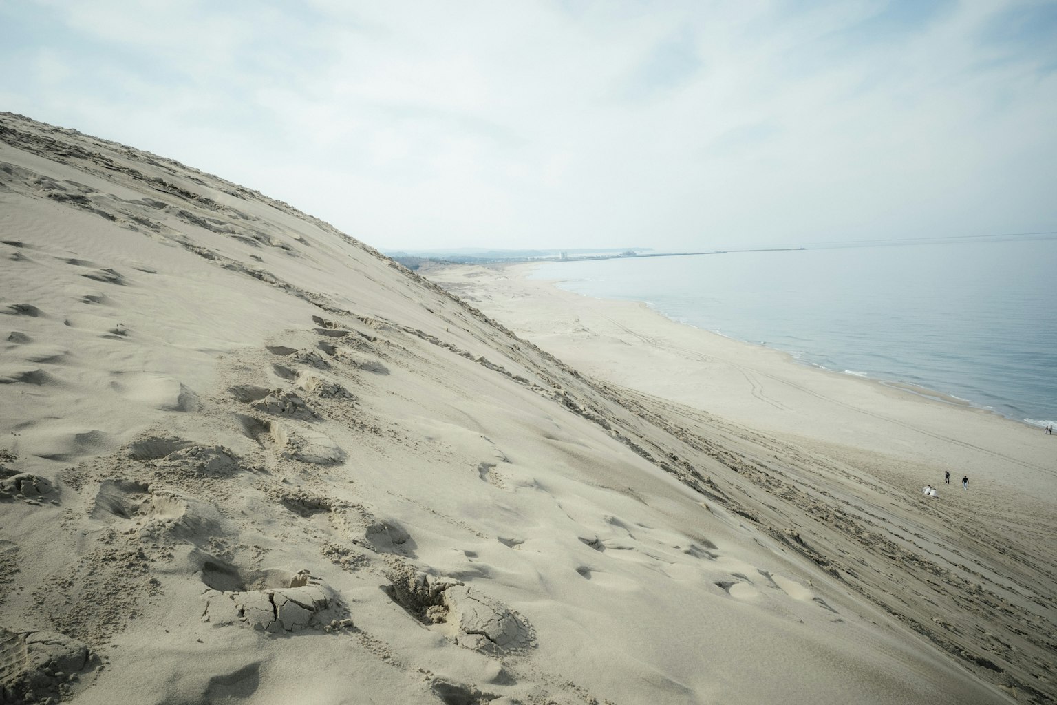 Pente de dune de sable menant à la plage sous un ciel nuageux