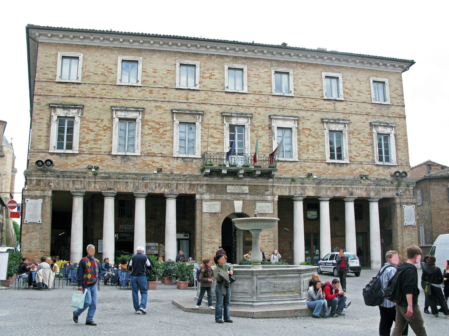Bâtiment classique avec des colonnes sur une place avec une fontaine et des gens