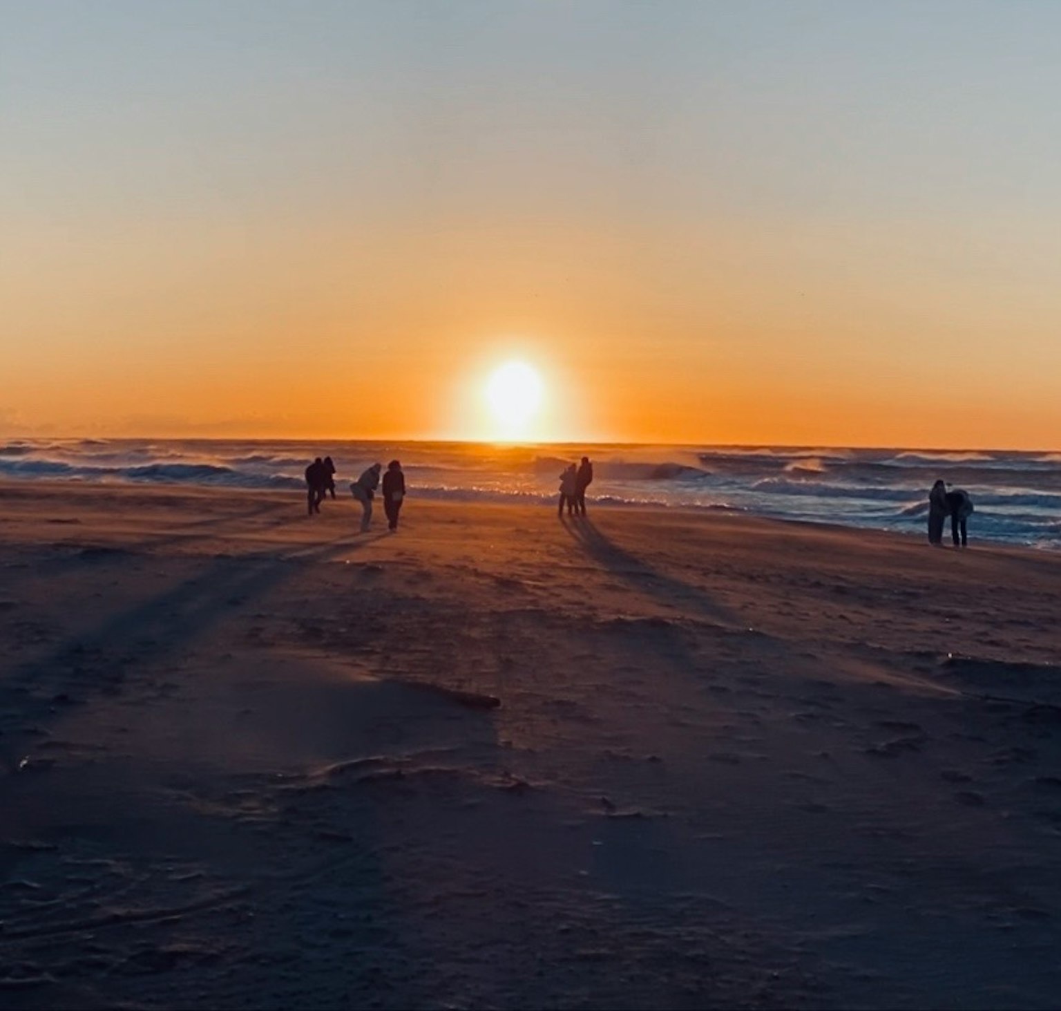 Scena di spiaggia con tramonto e silhouette di persone che camminano