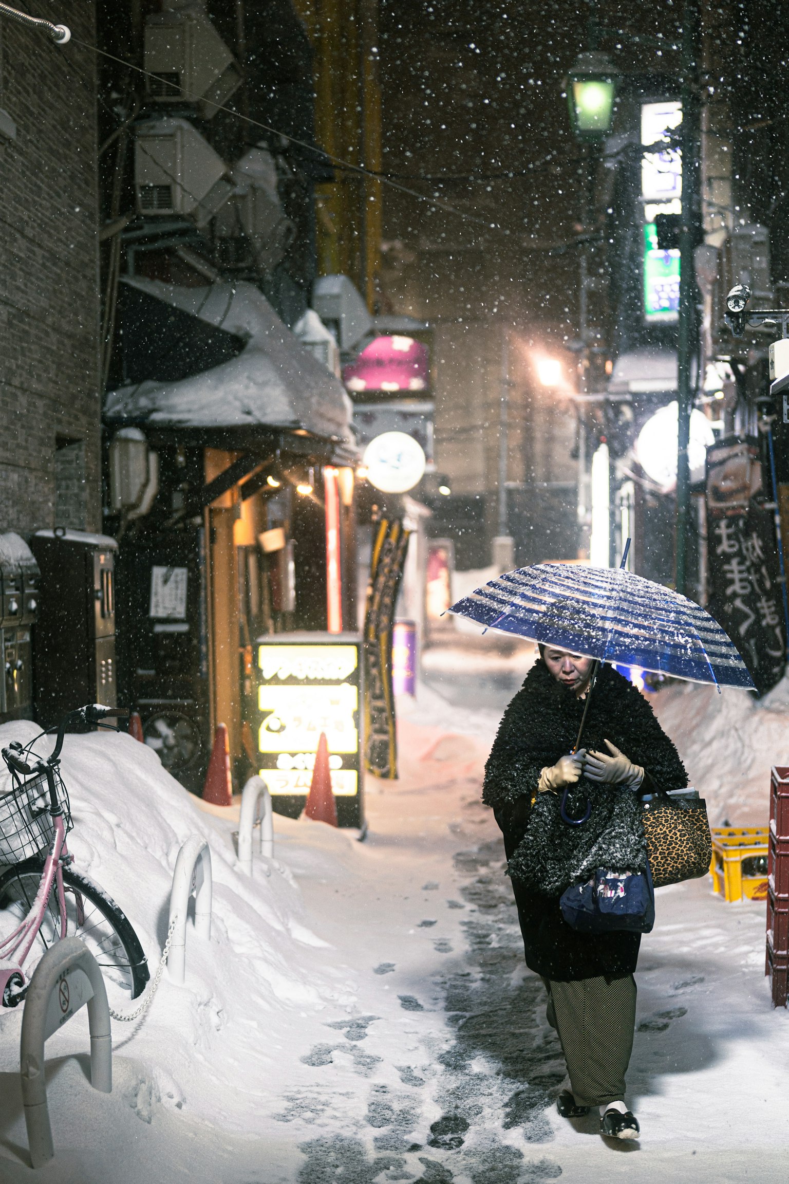 一位女性在雪中拿著雨傘走在狹窄的街道上