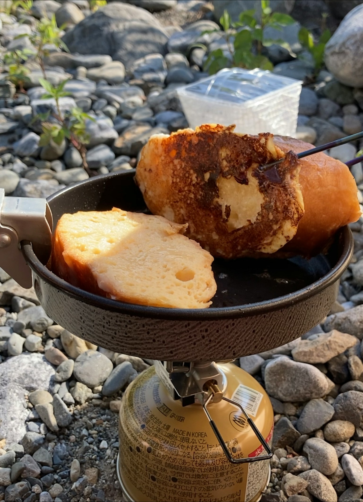 露营炉上的煎饼状食物，周围是卵石