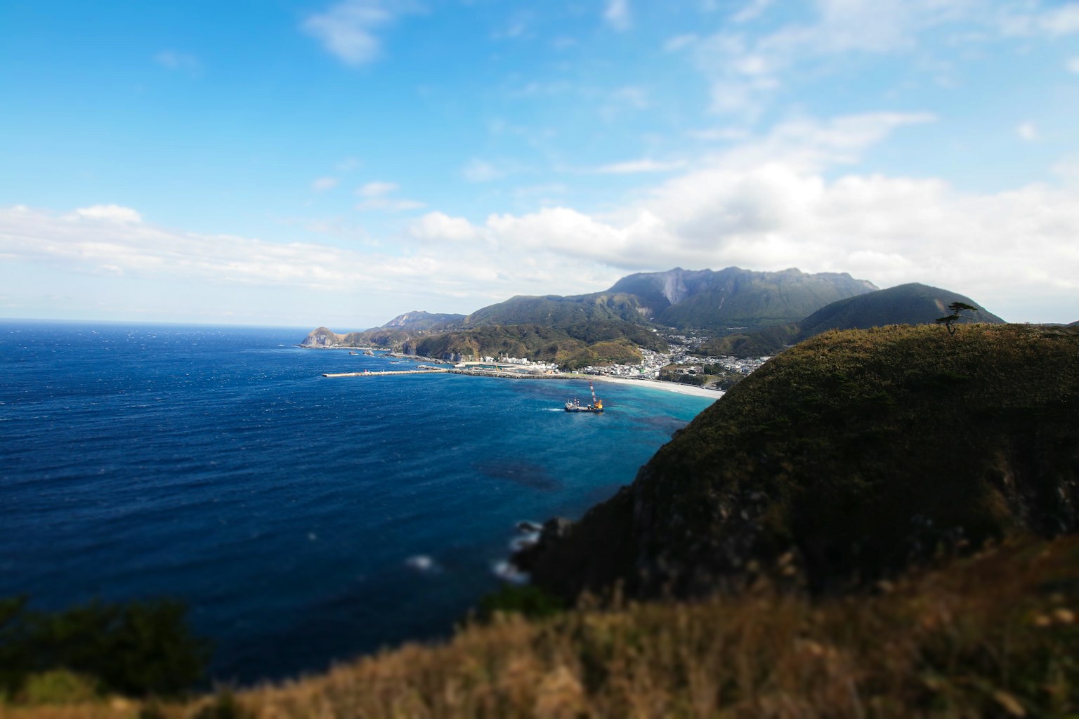 Vista panoramica dell'oceano blu e delle montagne sotto un cielo sereno, onde dolci, colline verdi, costa