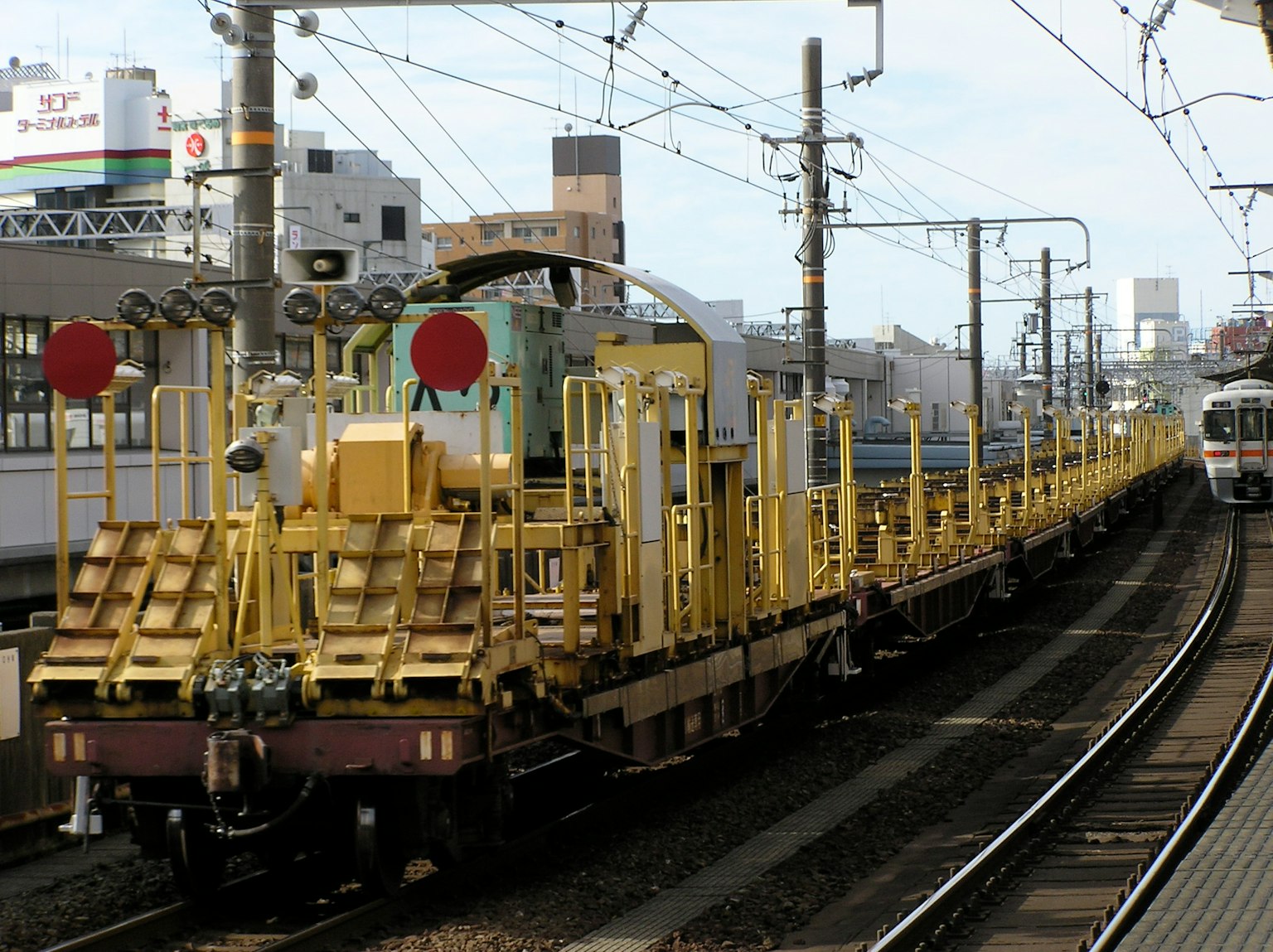 Un treno di manutenzione giallo che percorre i binari in un paesaggio urbano