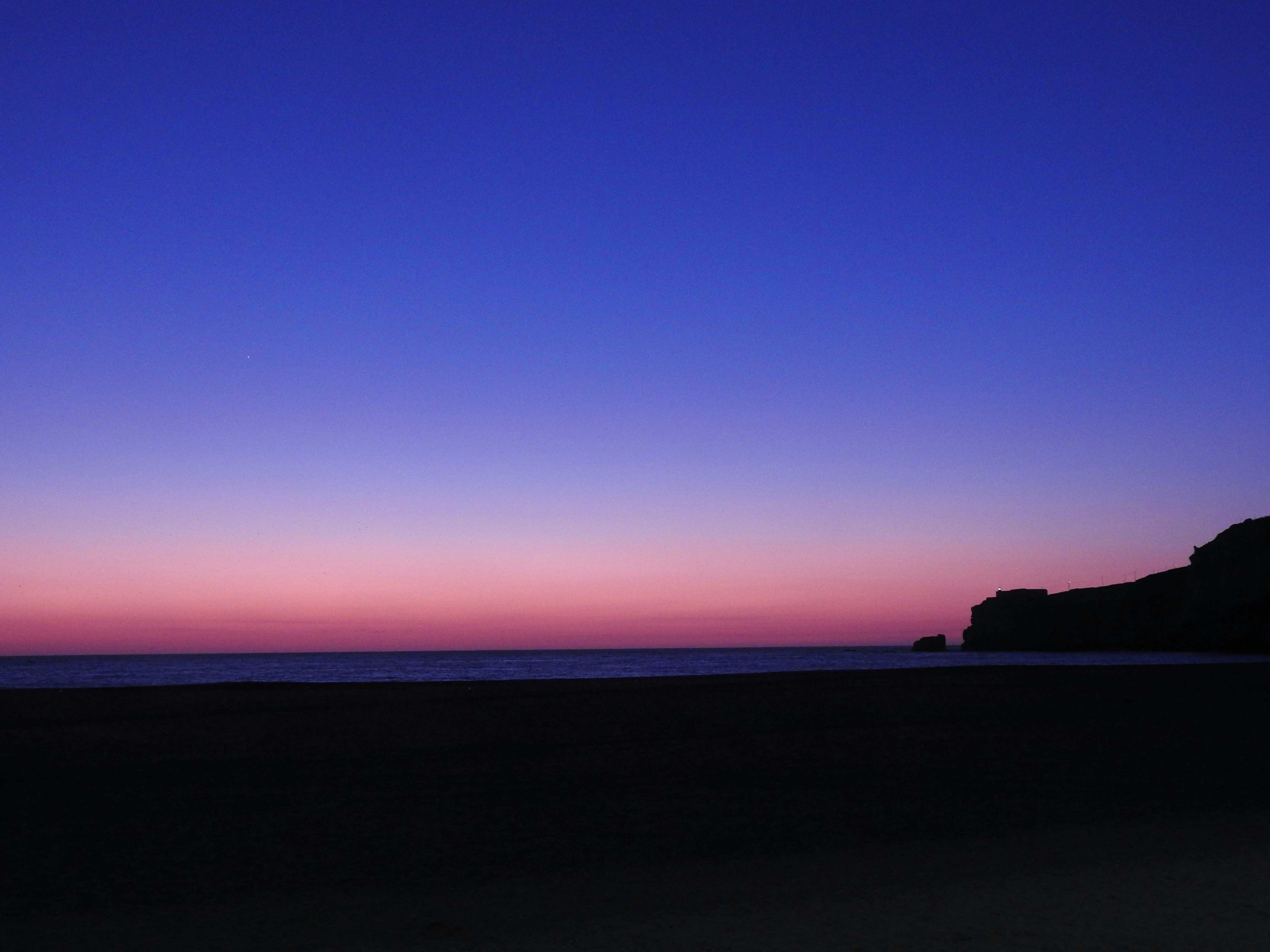 夕暮れの海と水平線、暗い海岸のシルエット