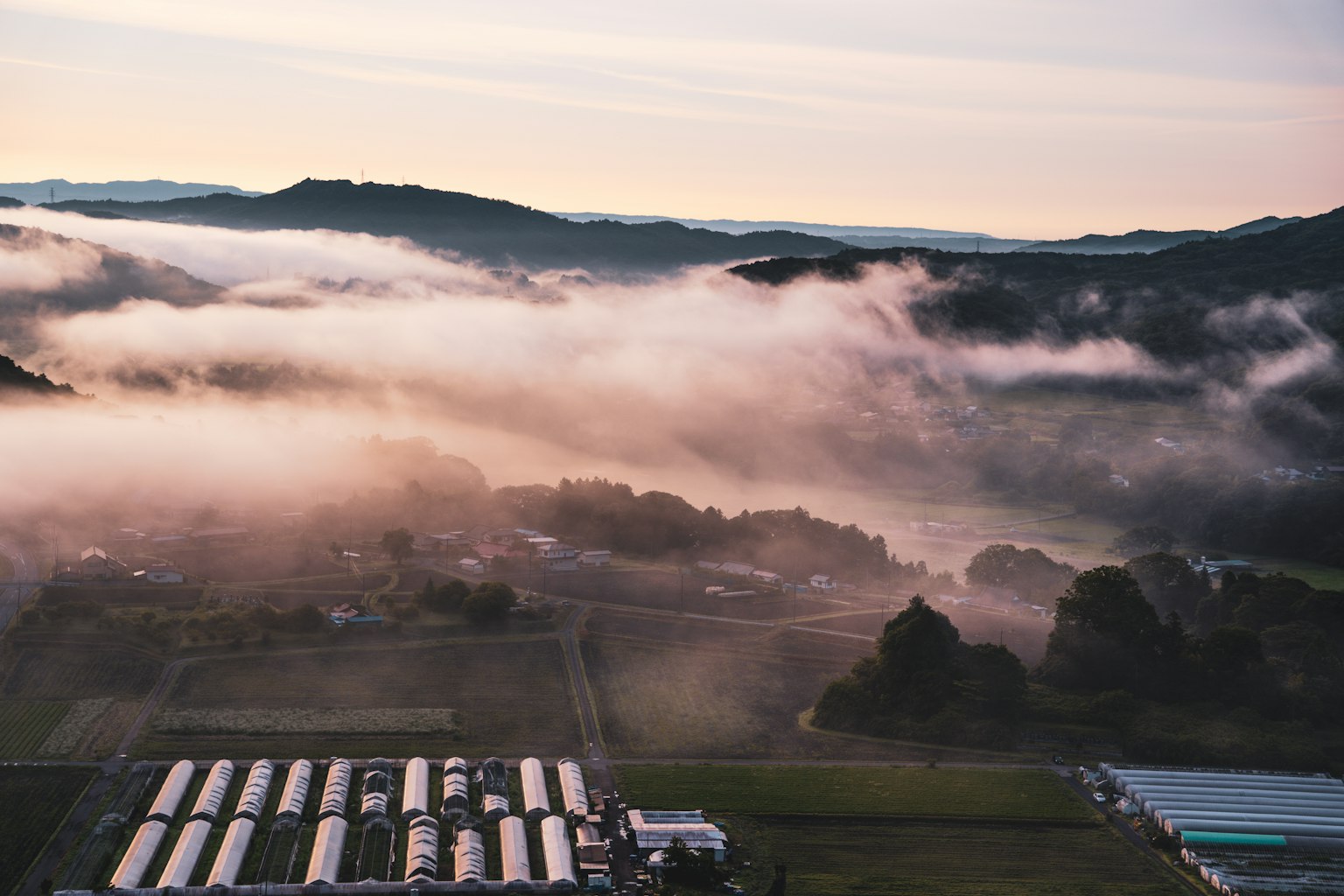 Vista aerea di montagne nebbiose e terreni agricoli all'alba