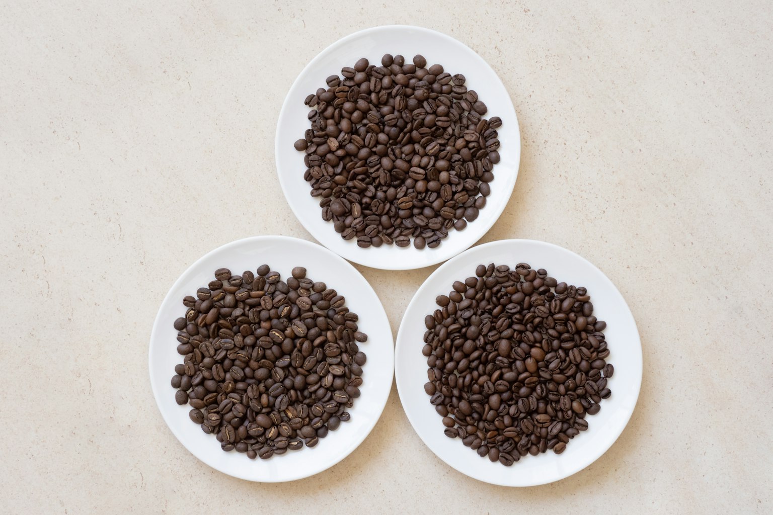 Trois assiettes blanches remplies de grains de café disposées en formation triangulaire