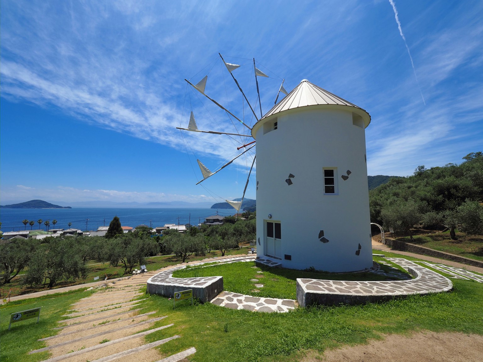 Vista escénica de un molino blanco contra un cielo azul y el mar