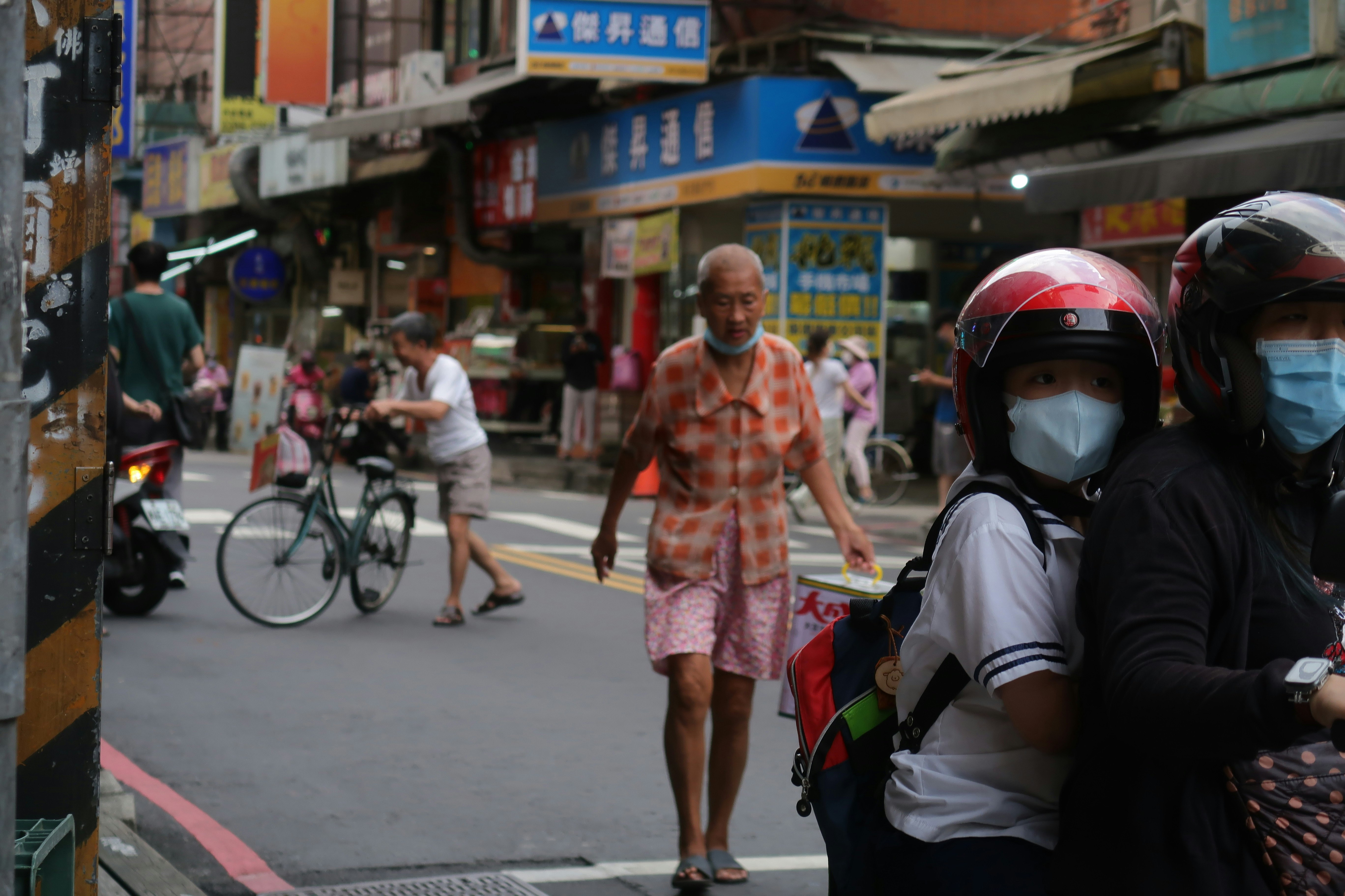 persone con la mascherina e scooter in una stretta via commerciale