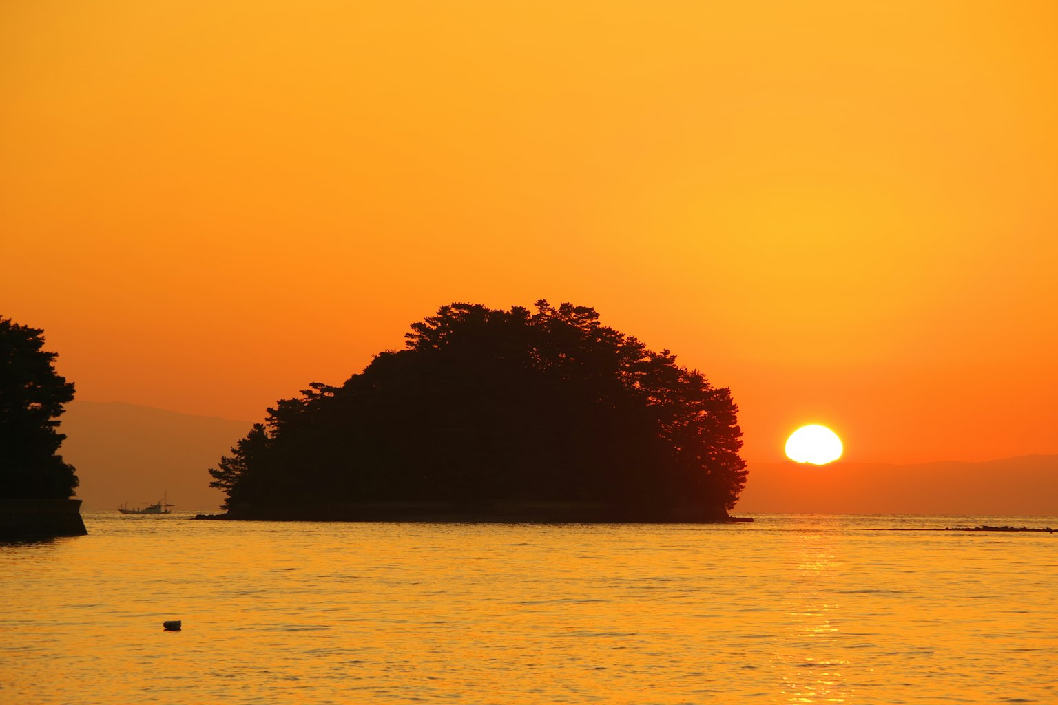 Silhouette einer Insel bei Sonnenuntergang über ruhigem Wasser