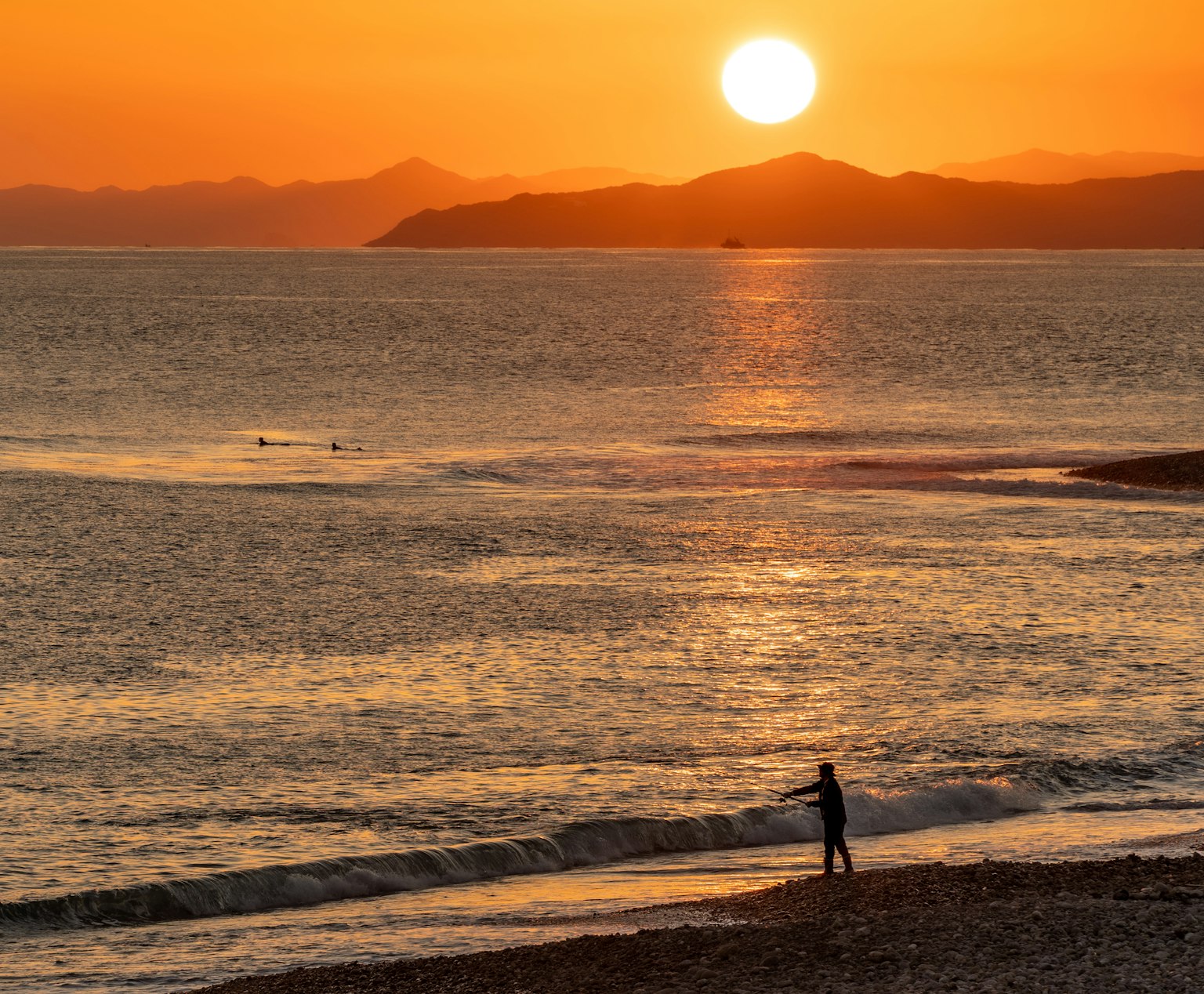 Une belle scène de plage avec un coucher de soleil orange sur l'océan et une personne debout au bord de l'eau