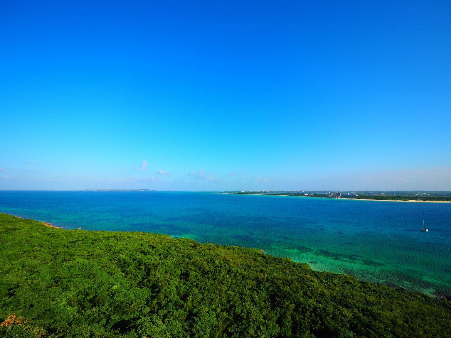 Langit biru luas di atas garis pantai hijau dengan air laut yang jernih