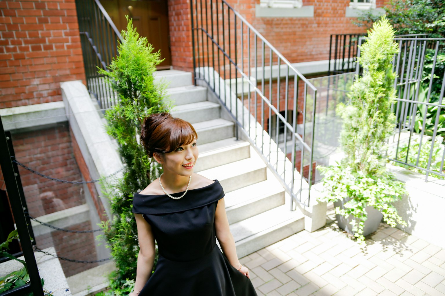 Mujer con vestido negro sonriendo cerca de plantas verdes