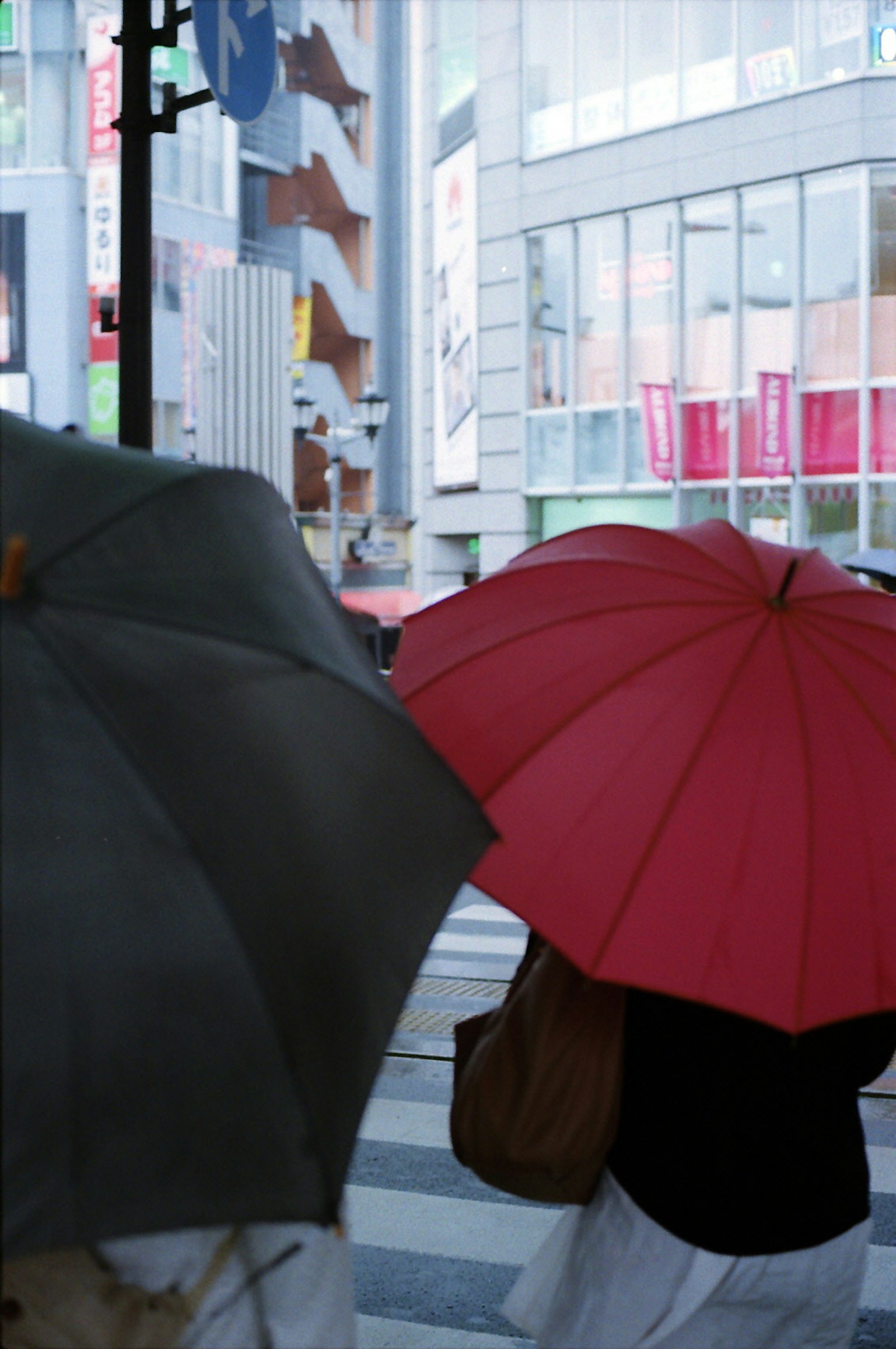 People crossing the street with umbrellas a prominent red umbrella and a gray umbrella