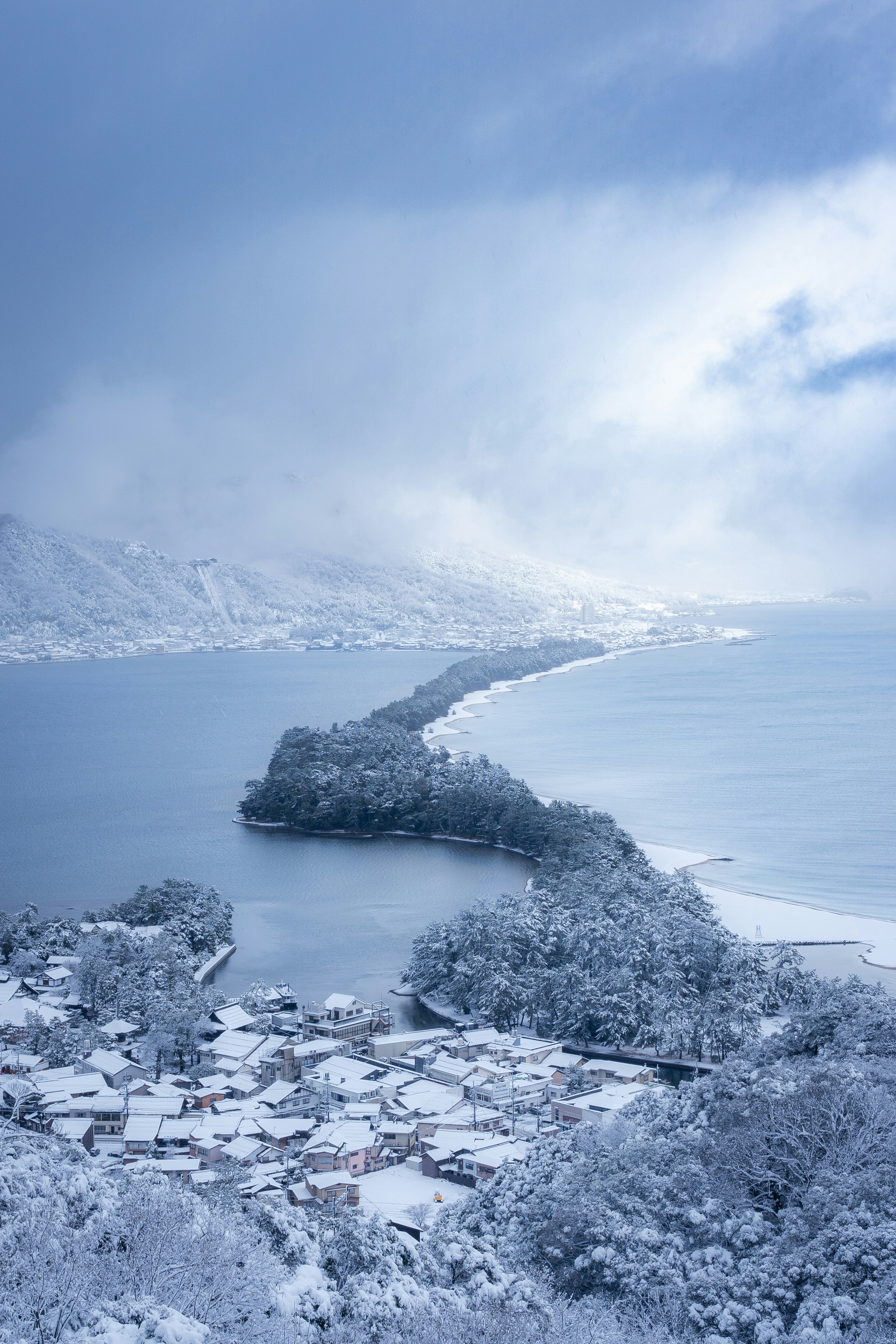 Snowy view of Amanohashidate with sea and pine-lined shore in winter