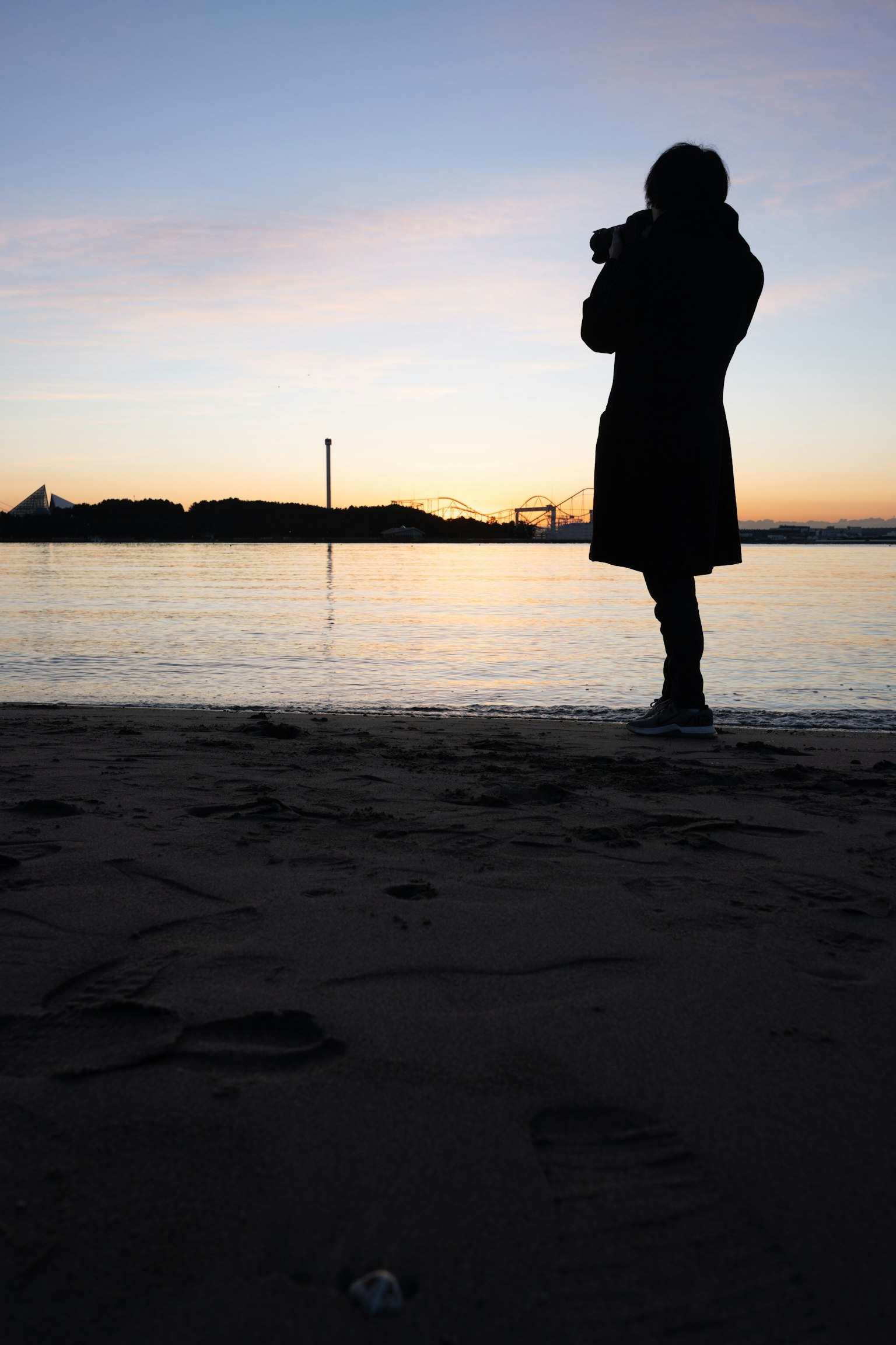 夕焼けの海辺でカメラを持つシルエットの人物