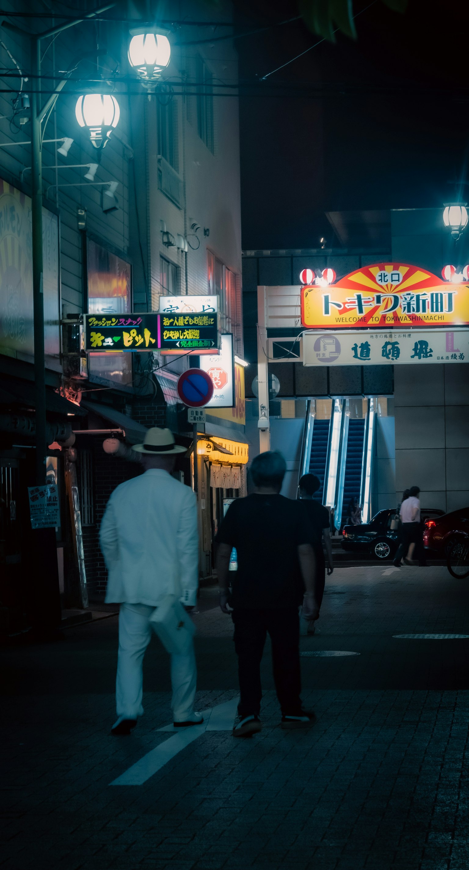 两名男子站在夜间街道上，一名穿白色西装，另一名穿黑色衣服