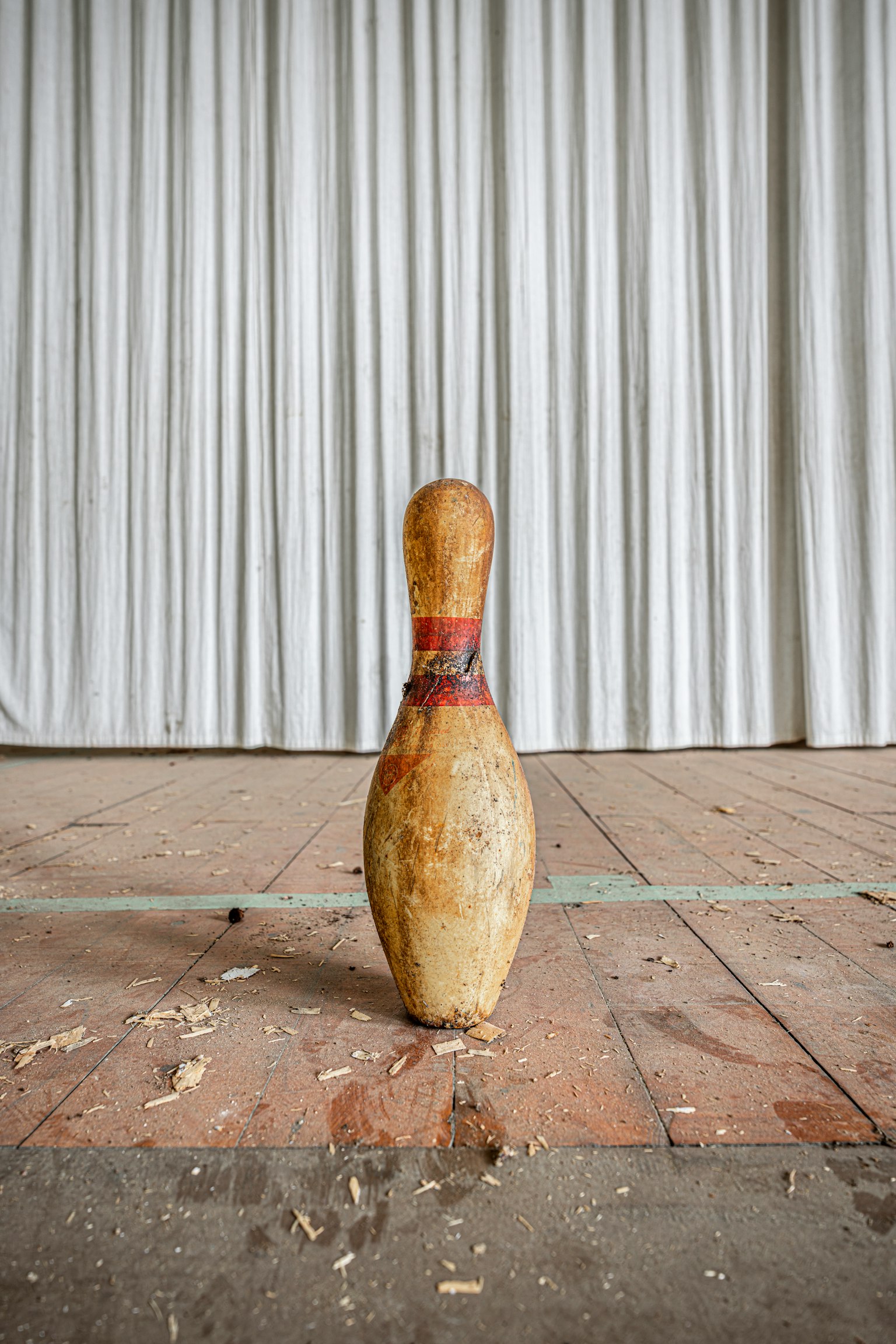 Un vecchio birillo da bowling in piedi su un pavimento di legno con uno sfondo di tenda bianca