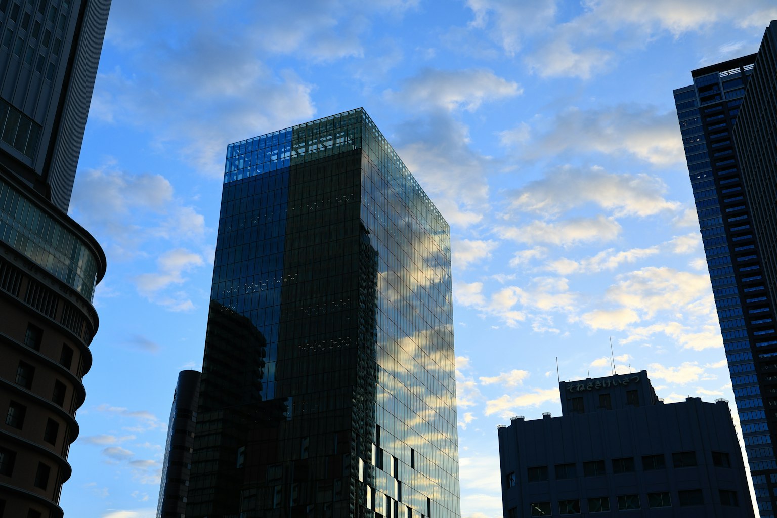 Un edificio alto que refleja el cielo azul y las nubes en un paisaje urbano