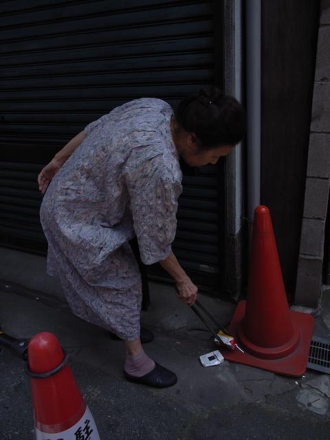 路地のシャッター前で作業する人とコーン
